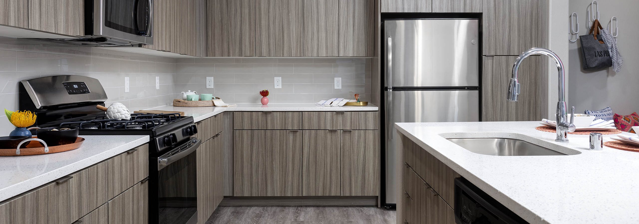 Interior view of AMLI Camarillo apartment kitchen with light wood grain cabinets, stainless appliances, quartz counters and tile backsplash