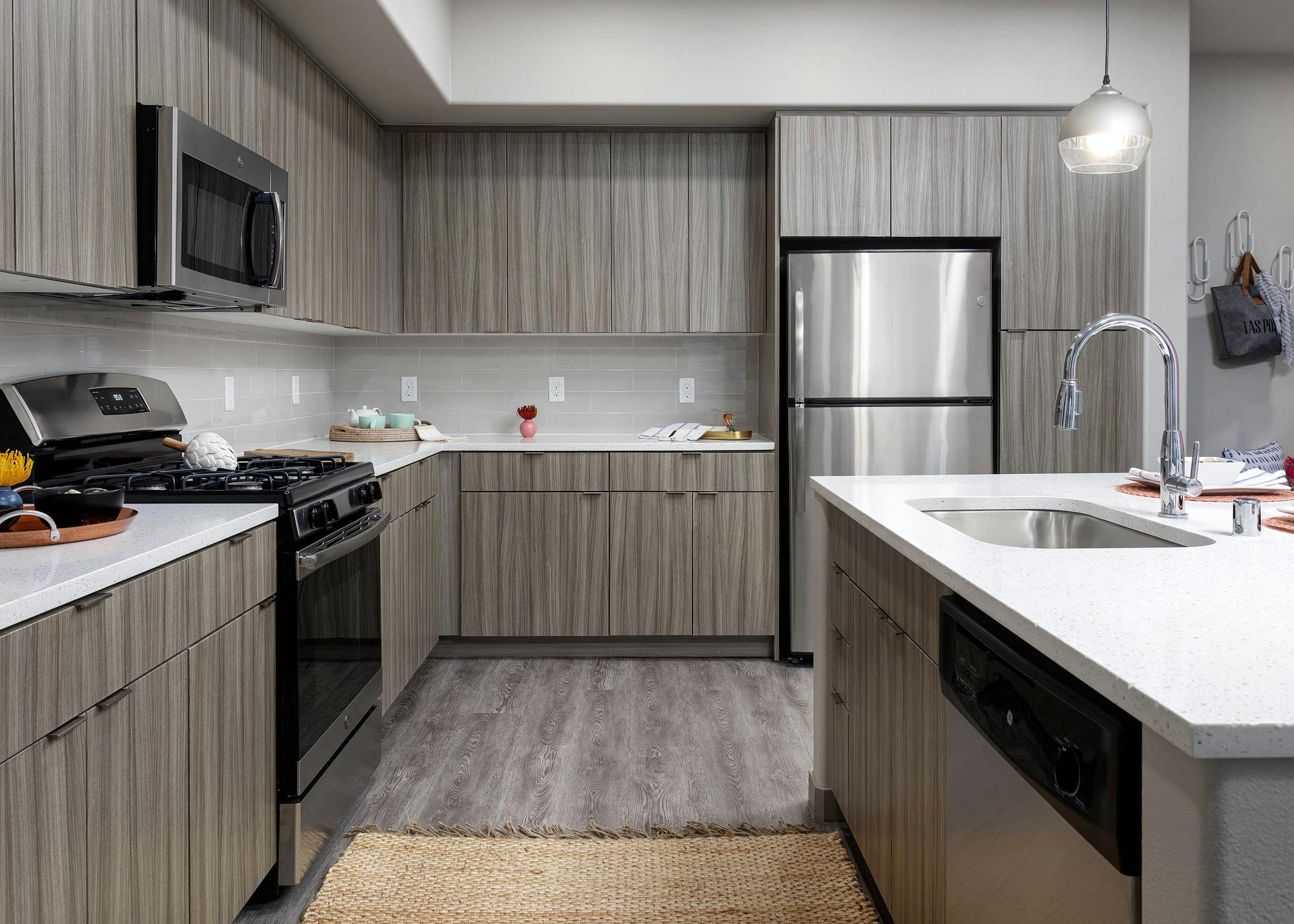 Interior view of AMLI Camarillo apartment kitchen with light wood grain cabinets, stainless appliances, quartz counters and tile backsplash