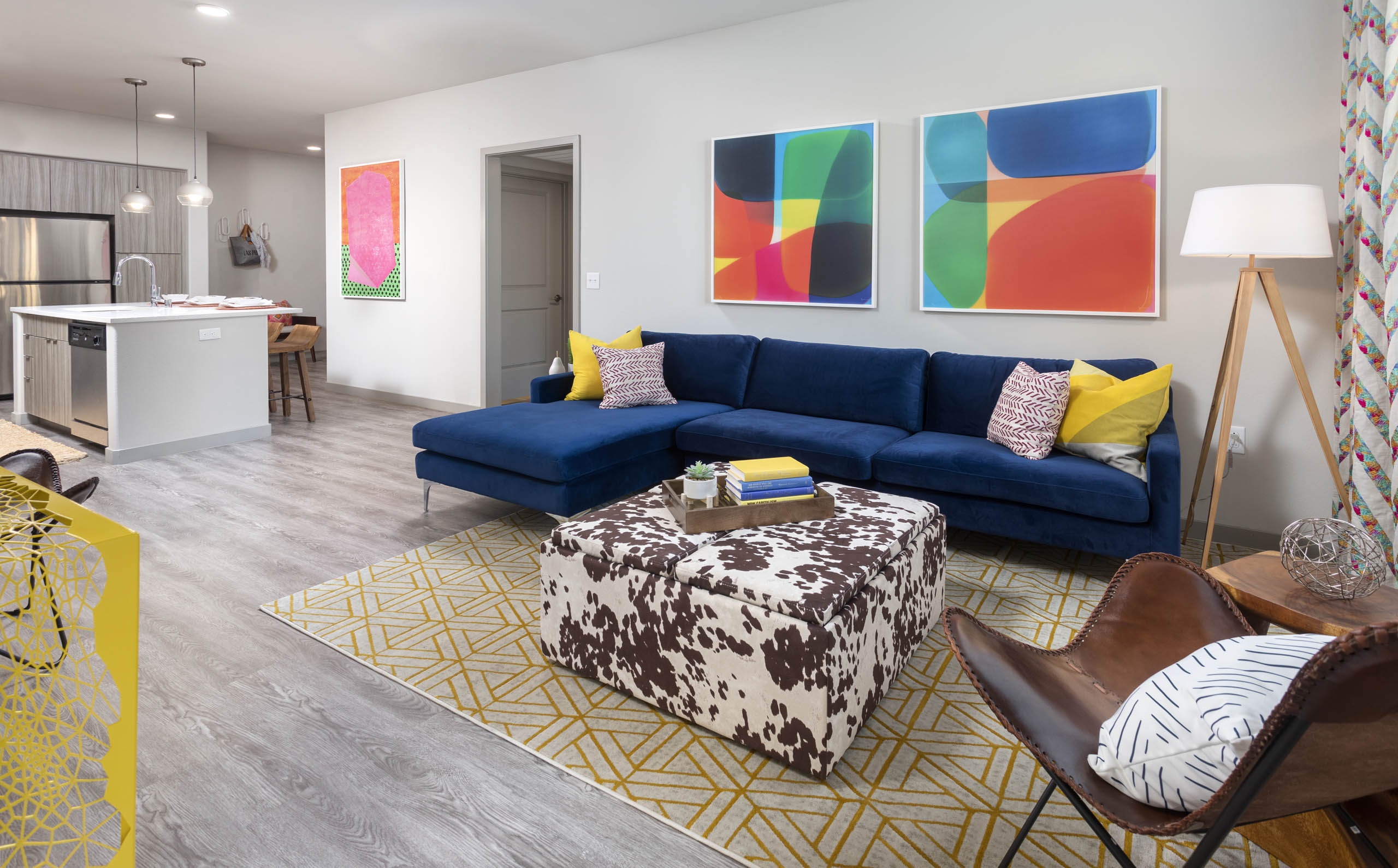 AMLI Camarillo open floor plan apartment living room with blue sofa, colorful decor, and view into modern kitchen with island seating