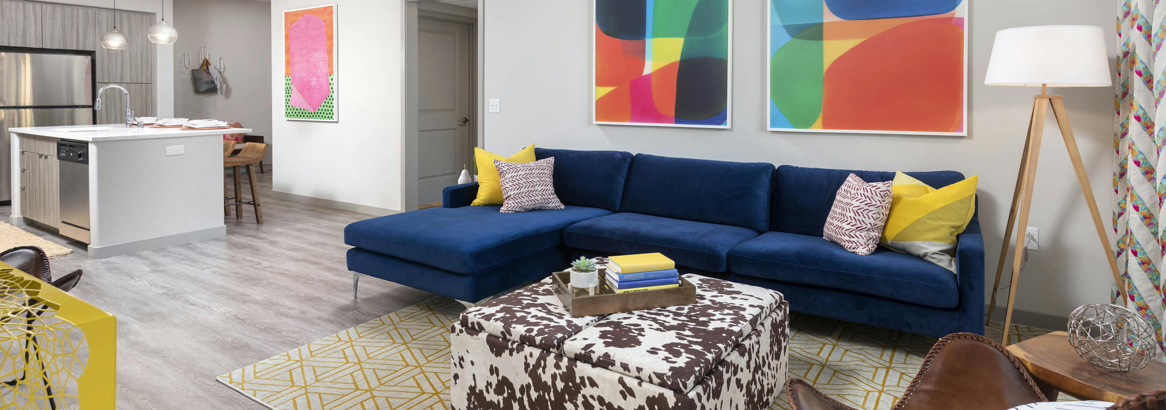 AMLI Camarillo open floor plan apartment living room with blue sofa, colorful decor, and view into modern kitchen with island seating