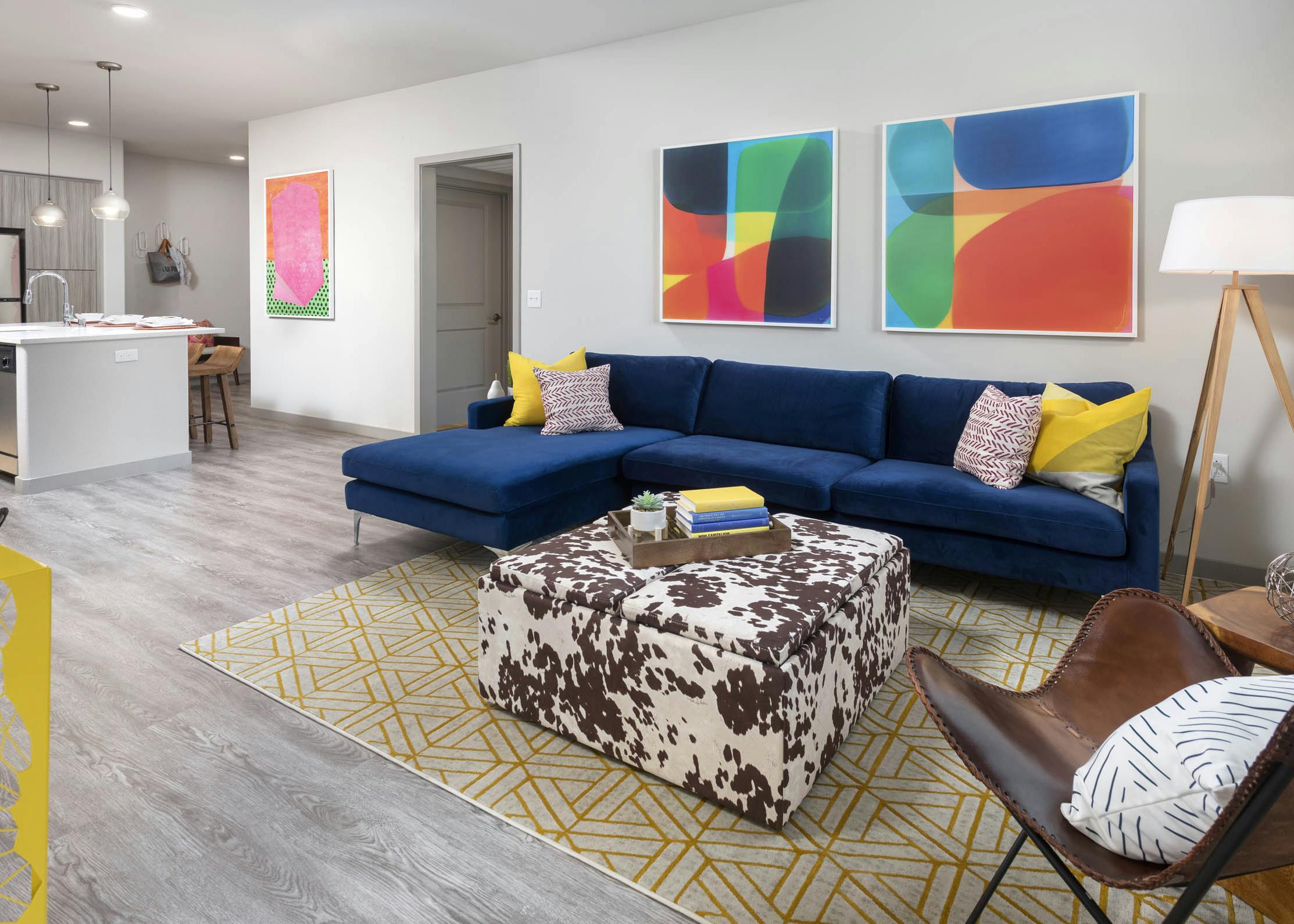 AMLI Camarillo open floor plan apartment living room with blue sofa, colorful decor, and view into modern kitchen with island seating