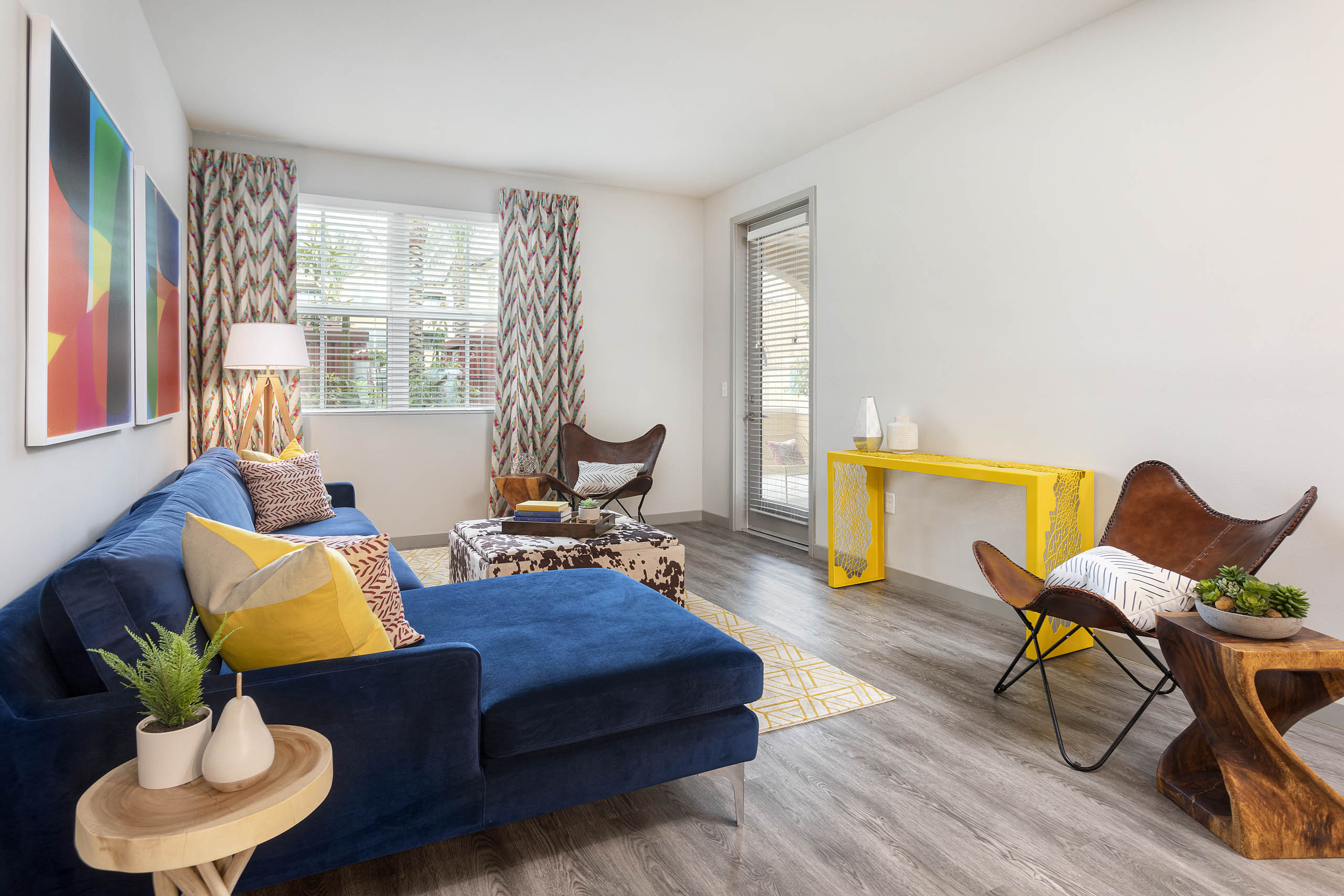 Interior view of AMLI Camarillo apartment living room with blue sofa, patterned drapes, accent chairs and wood-style floors