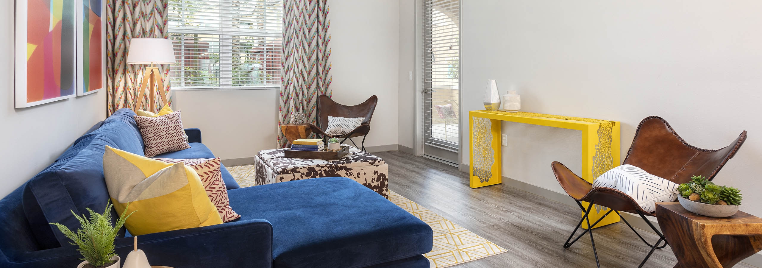 Interior view of AMLI Camarillo apartment living room with blue sofa, patterned drapes, accent chairs and wood-style floors