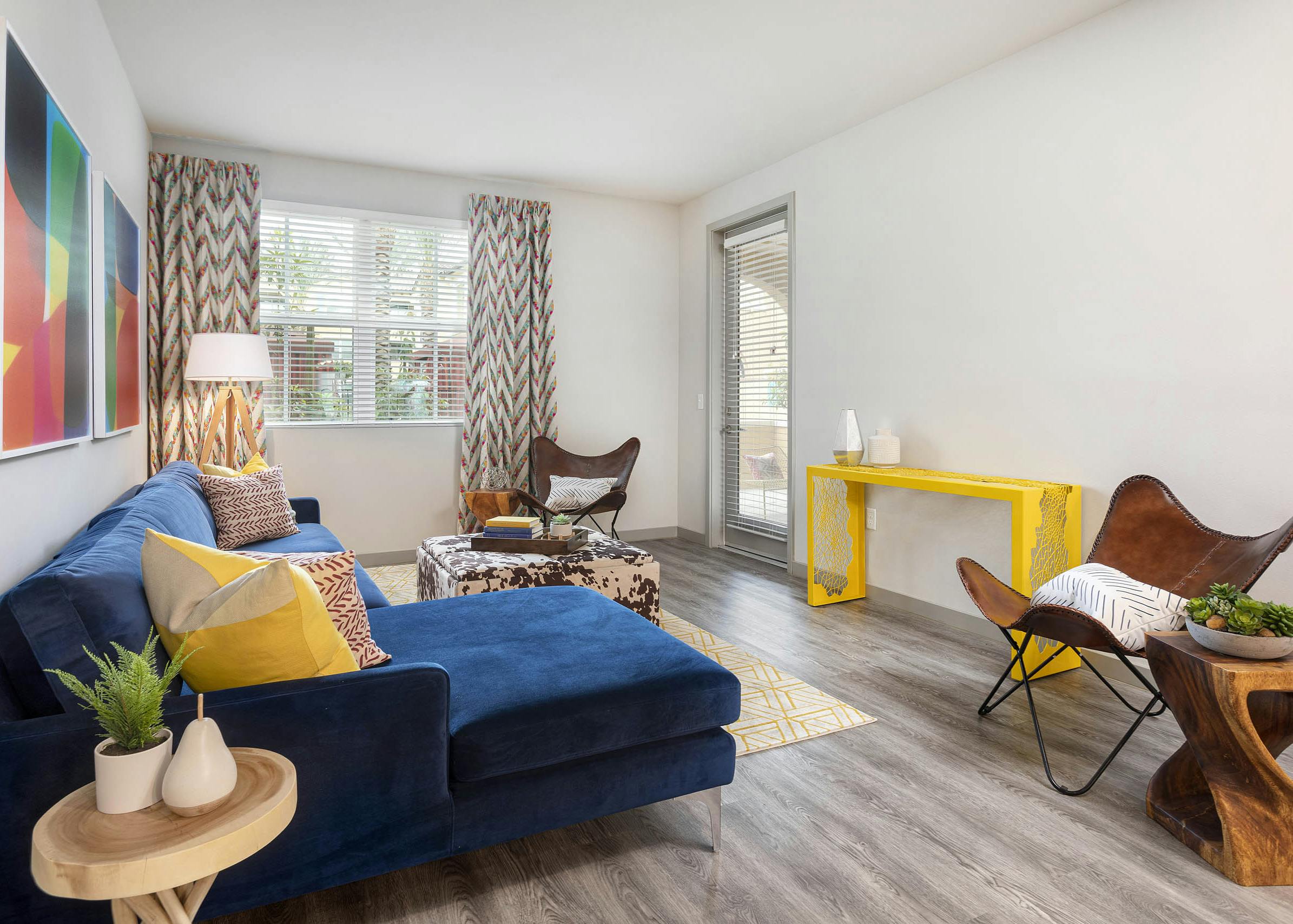 Interior view of AMLI Camarillo apartment living room with blue sofa, patterned drapes, accent chairs and wood-style floors