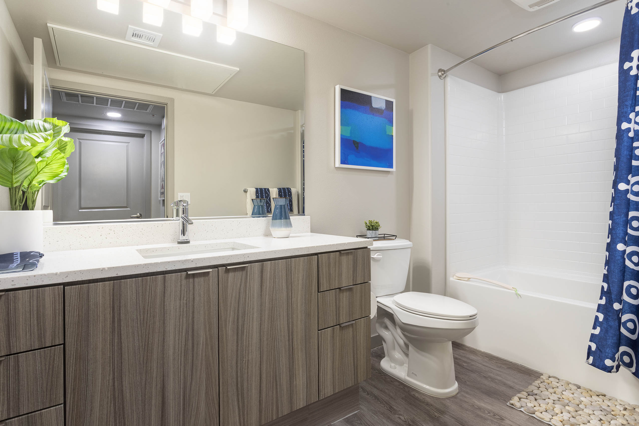 Bathroom with light wood grain cabinets, white quartz counters, and a tub/shower with tile surround at AMLI Camarillo apartments.