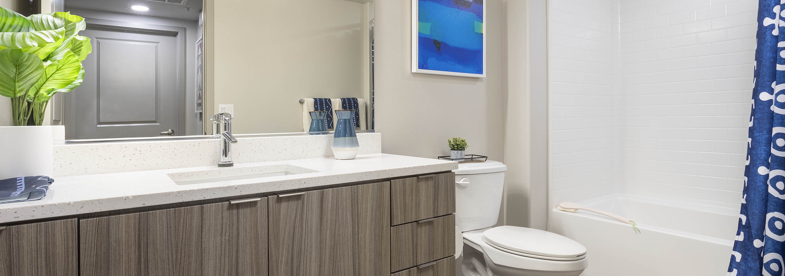 Bathroom with light wood grain cabinets, white quartz counters, and a tub/shower with tile surround at AMLI Camarillo apartments.