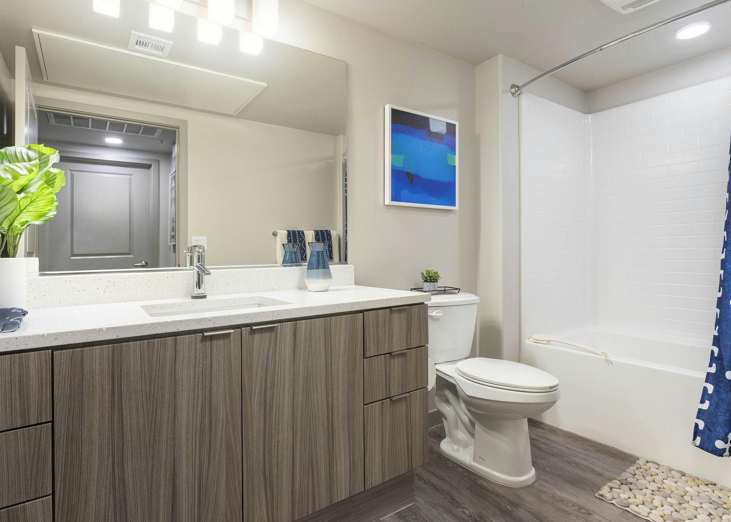 Bathroom with light wood grain cabinets, white quartz counters, and a tub/shower with tile surround at AMLI Camarillo apartments.