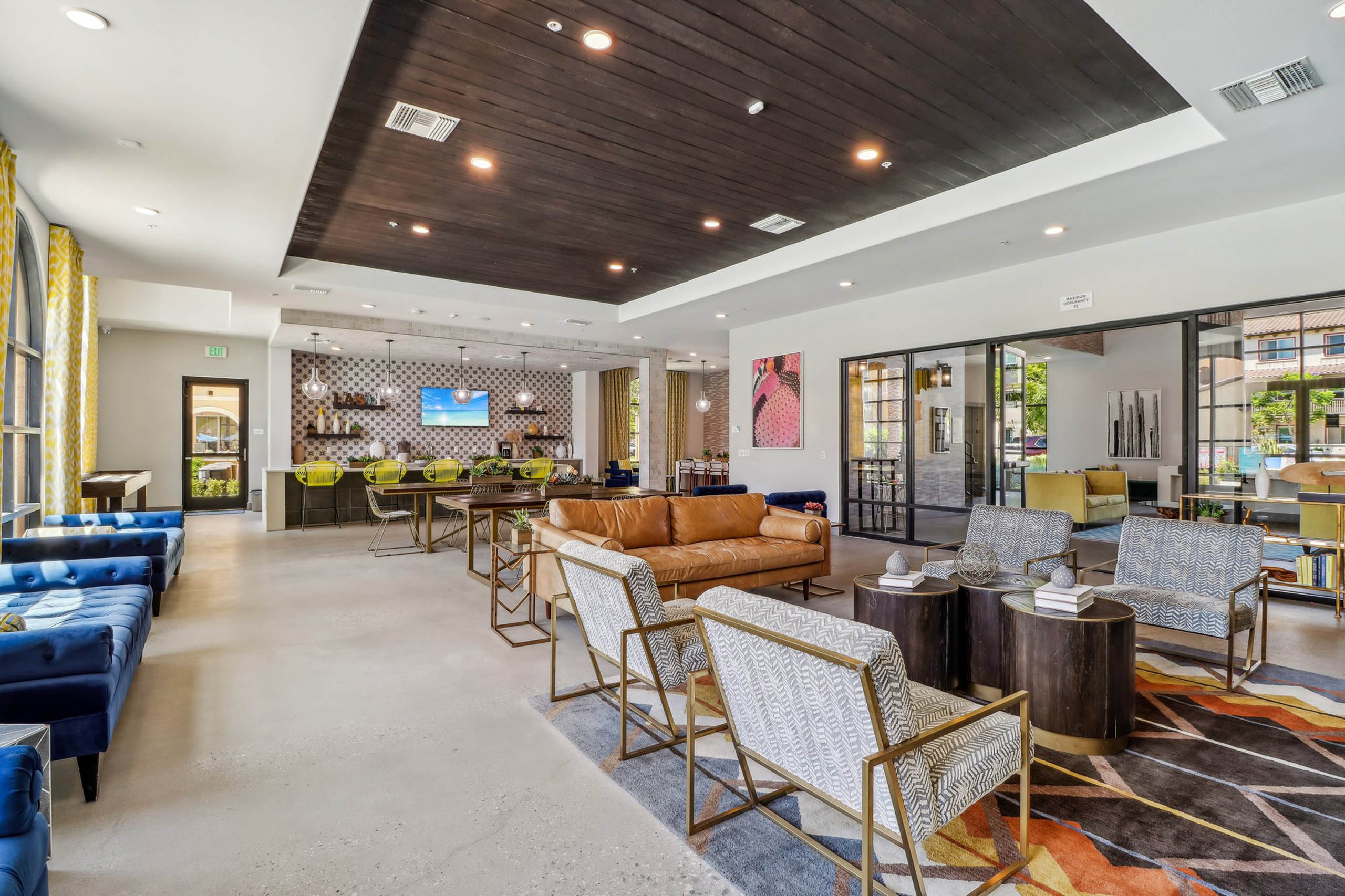 AMLI Camarillo apartment clubhouse with patterned rug, blue and leather seating, yellow barstools and a coffee bar along tiled wall