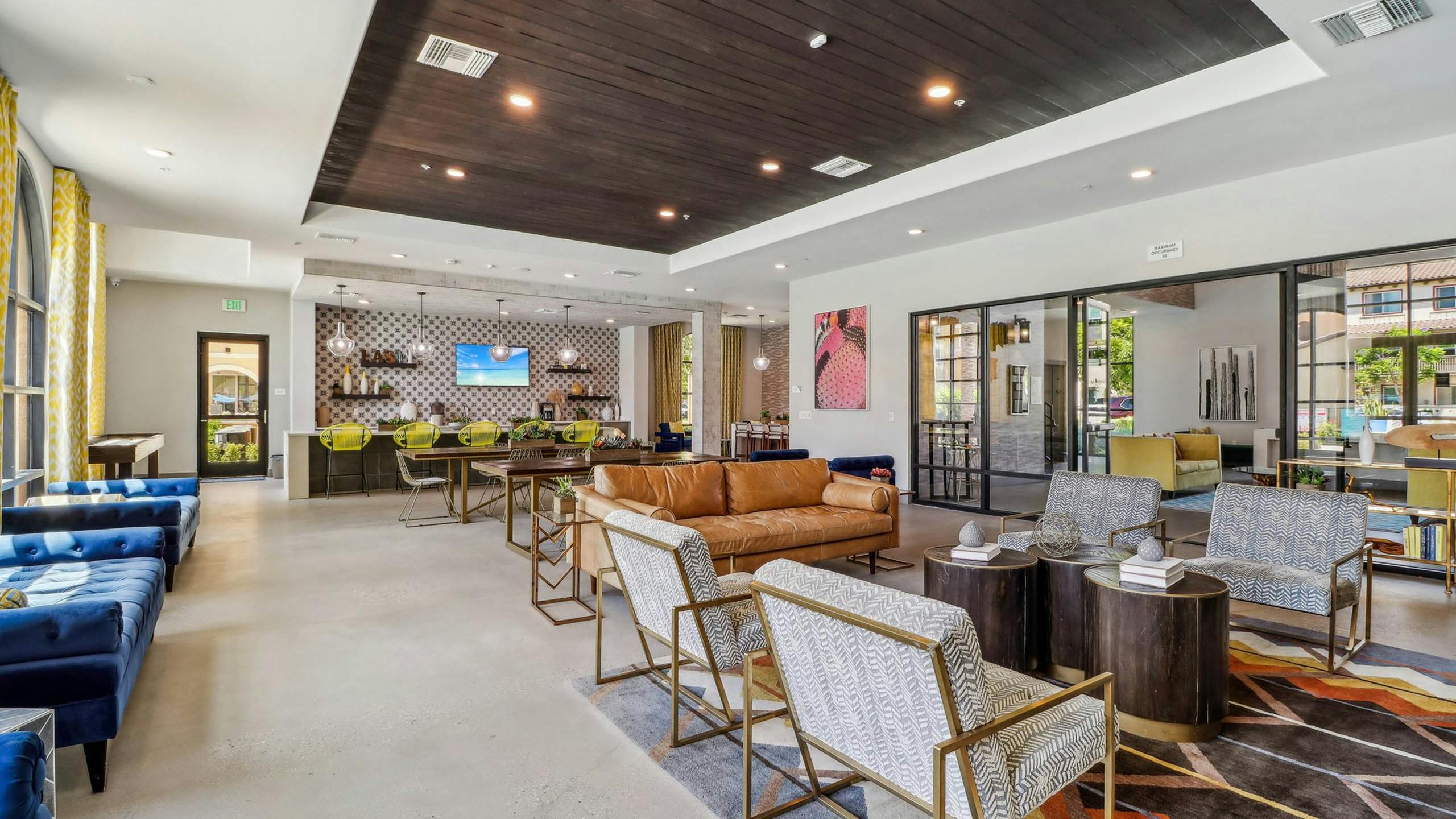 AMLI Camarillo apartment clubhouse with patterned rug, blue and leather seating, yellow barstools and a coffee bar along tiled wall