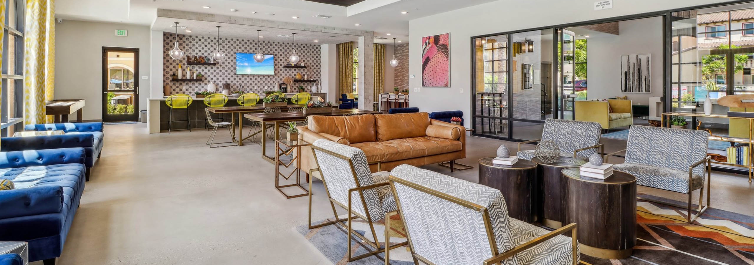 AMLI Camarillo apartment clubhouse with patterned rug, blue and leather seating, yellow barstools and a coffee bar along tiled wall