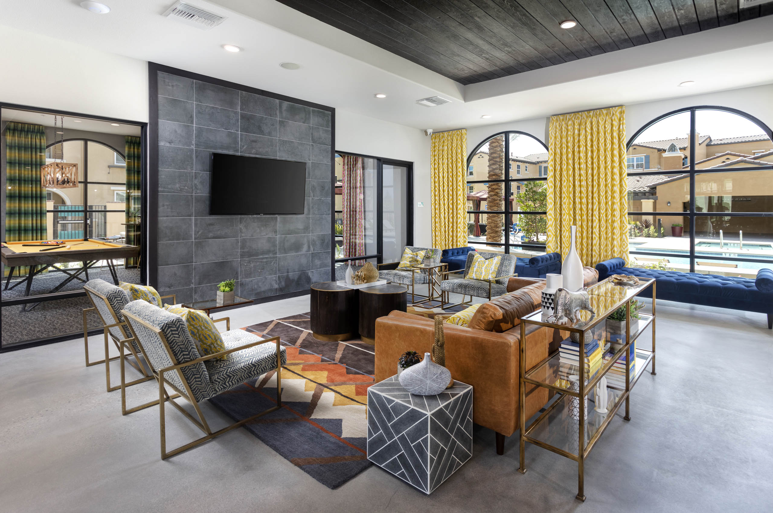 Interior view of AMLI Camarillo clubhouse lounge with bold decor, leather seating, mounted TV, and large windows overlooking the pool