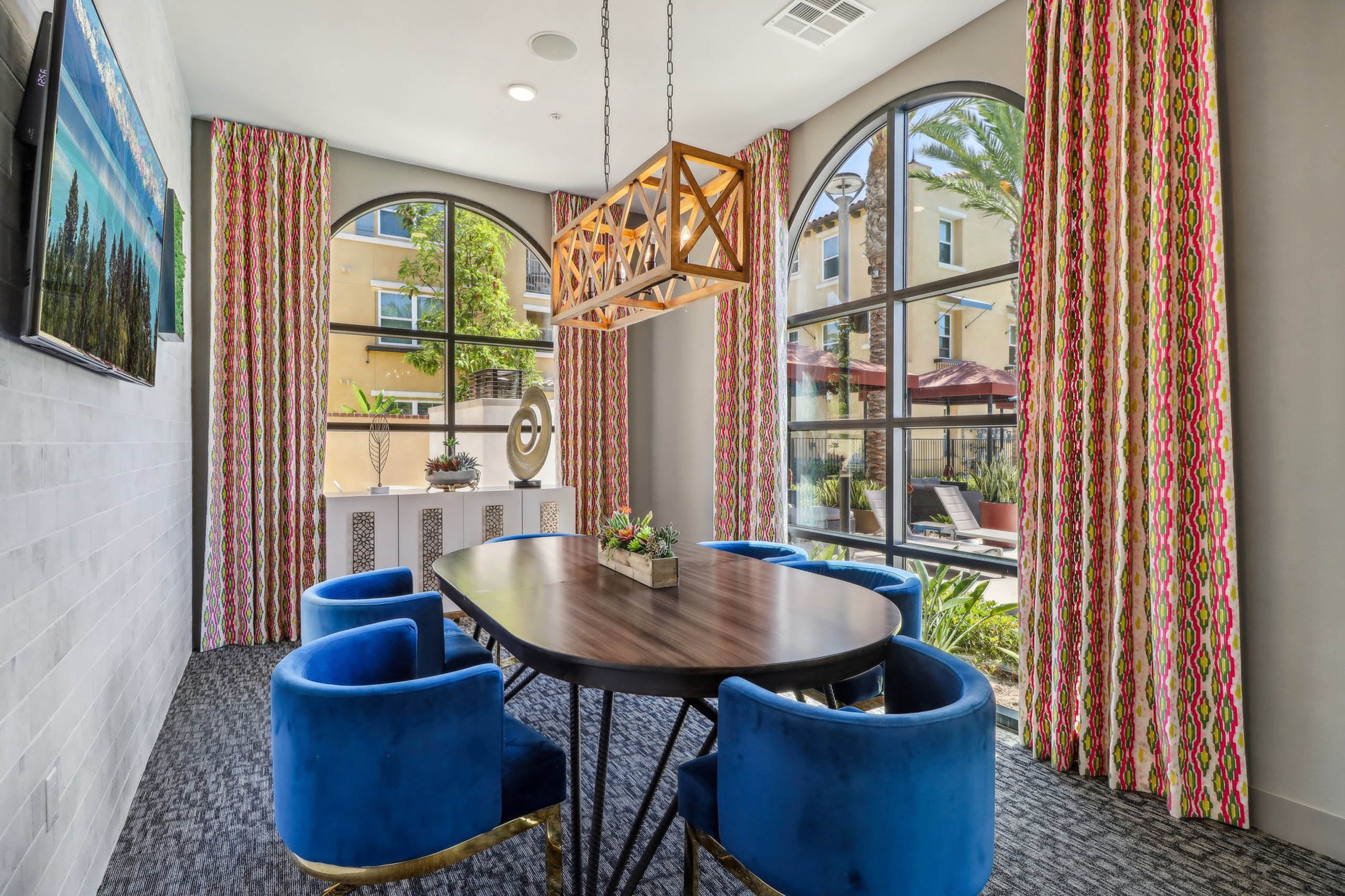 Private conference room at AMLI Camarillo apartments with blue velvet chairs, oval table, arched windows, patterned curtains and sculptural lighting