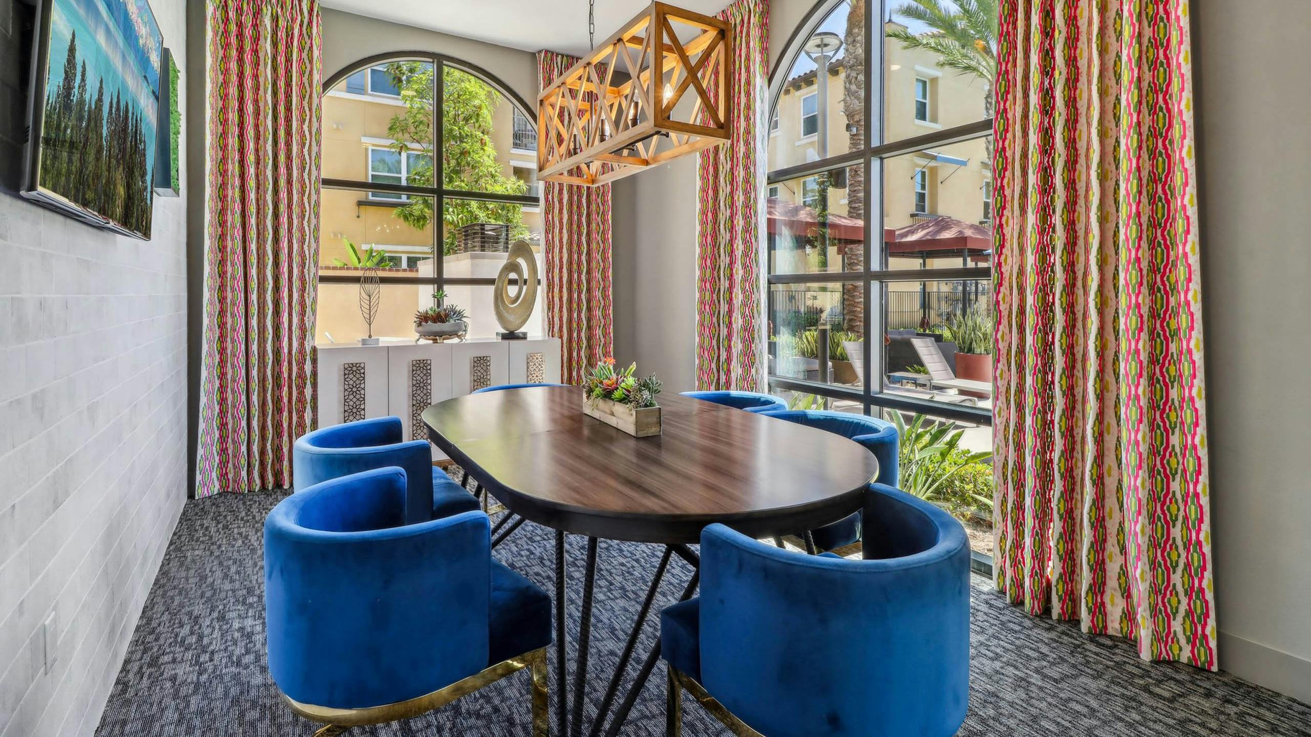 Private conference room at AMLI Camarillo apartments with blue velvet chairs, oval table, arched windows, patterned curtains and sculptural lighting