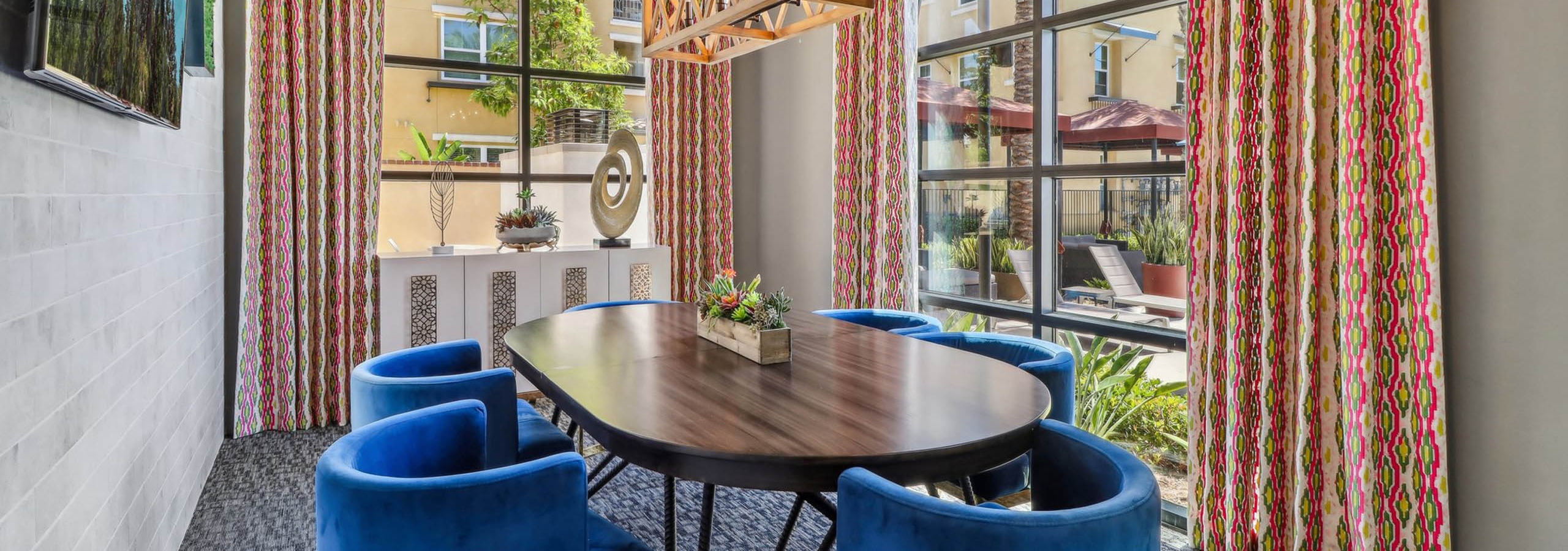Private conference room at AMLI Camarillo apartments with blue velvet chairs, oval table, arched windows, patterned curtains and sculptural lighting