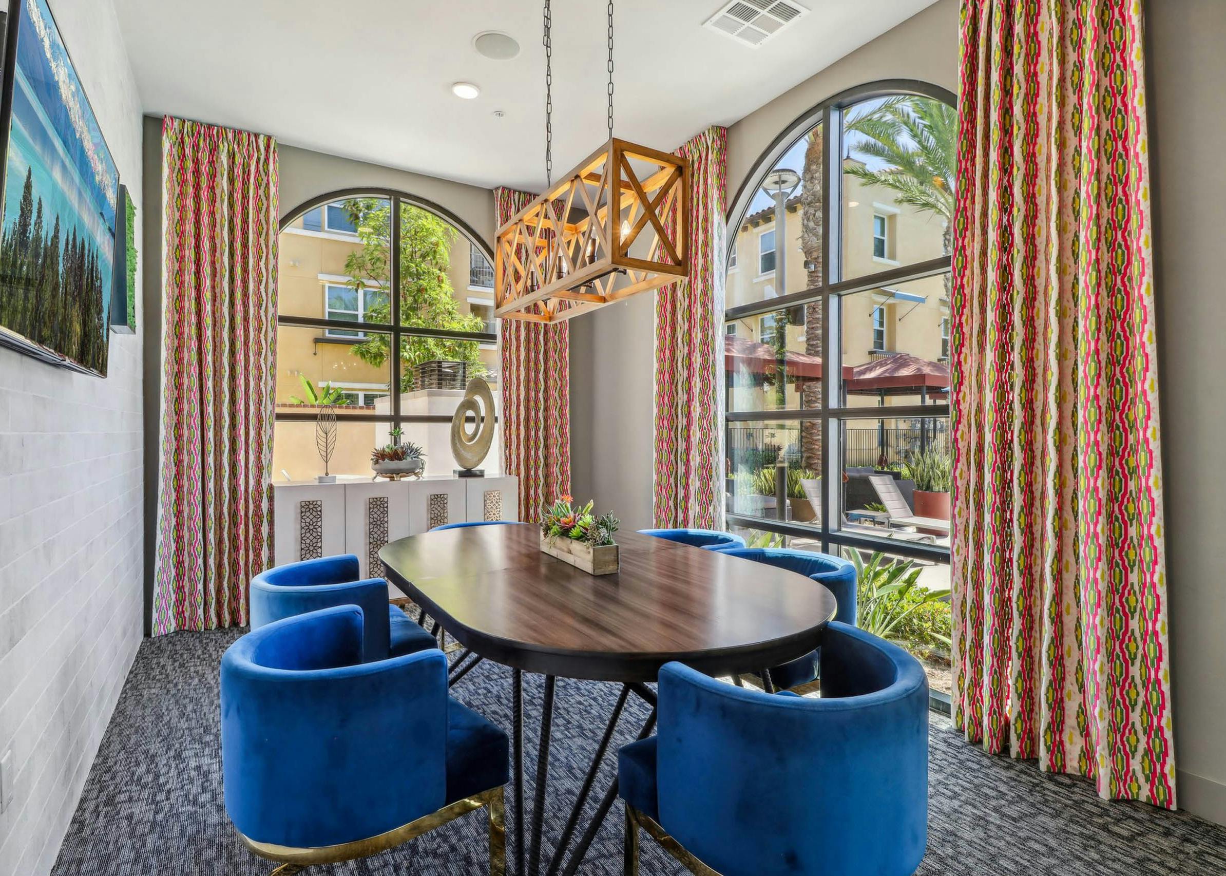 Private conference room at AMLI Camarillo apartments with blue velvet chairs, oval table, arched windows, patterned curtains and sculptural lighting