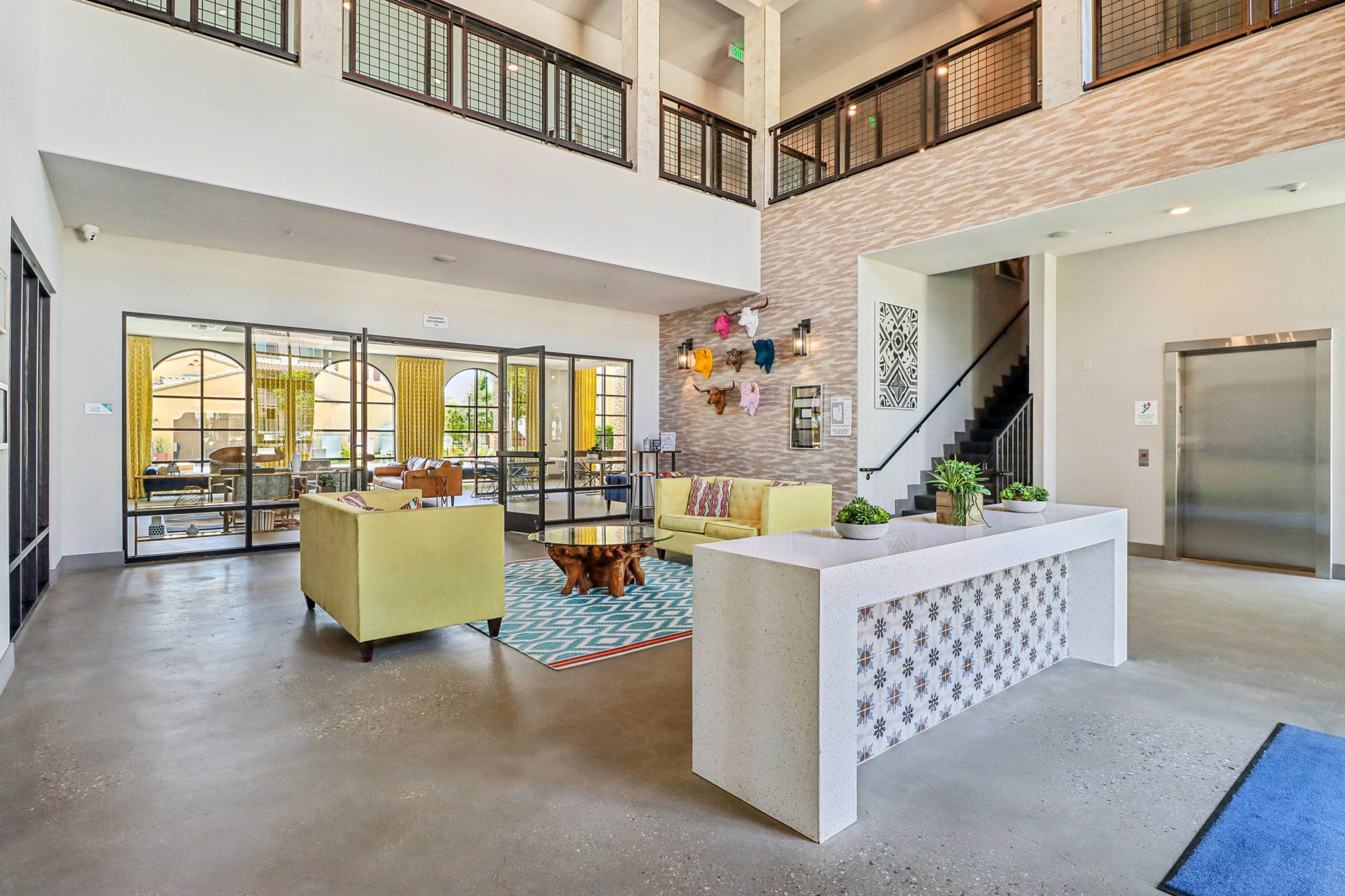 Interior lobby at AMLI Camarillo apartments featuring yellow seating, modern decor, double-height ceiling and a colorful lounge beyond