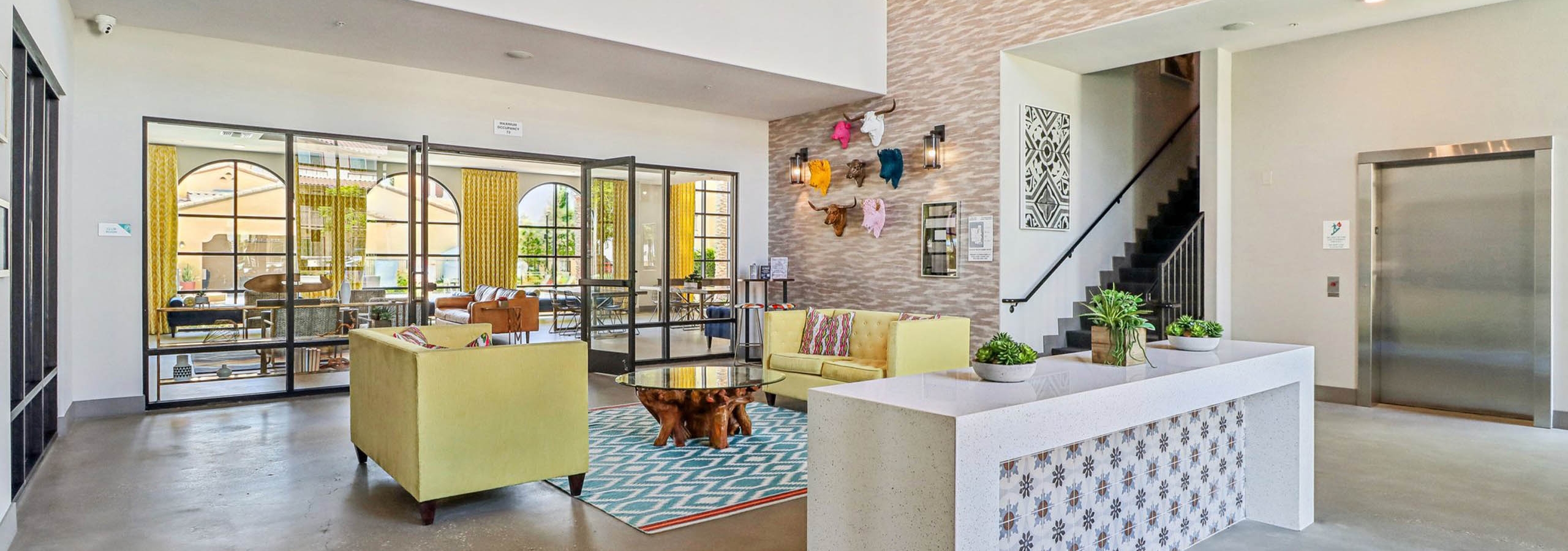 Interior lobby at AMLI Camarillo apartments featuring yellow seating, modern decor, double-height ceiling and a colorful lounge beyond