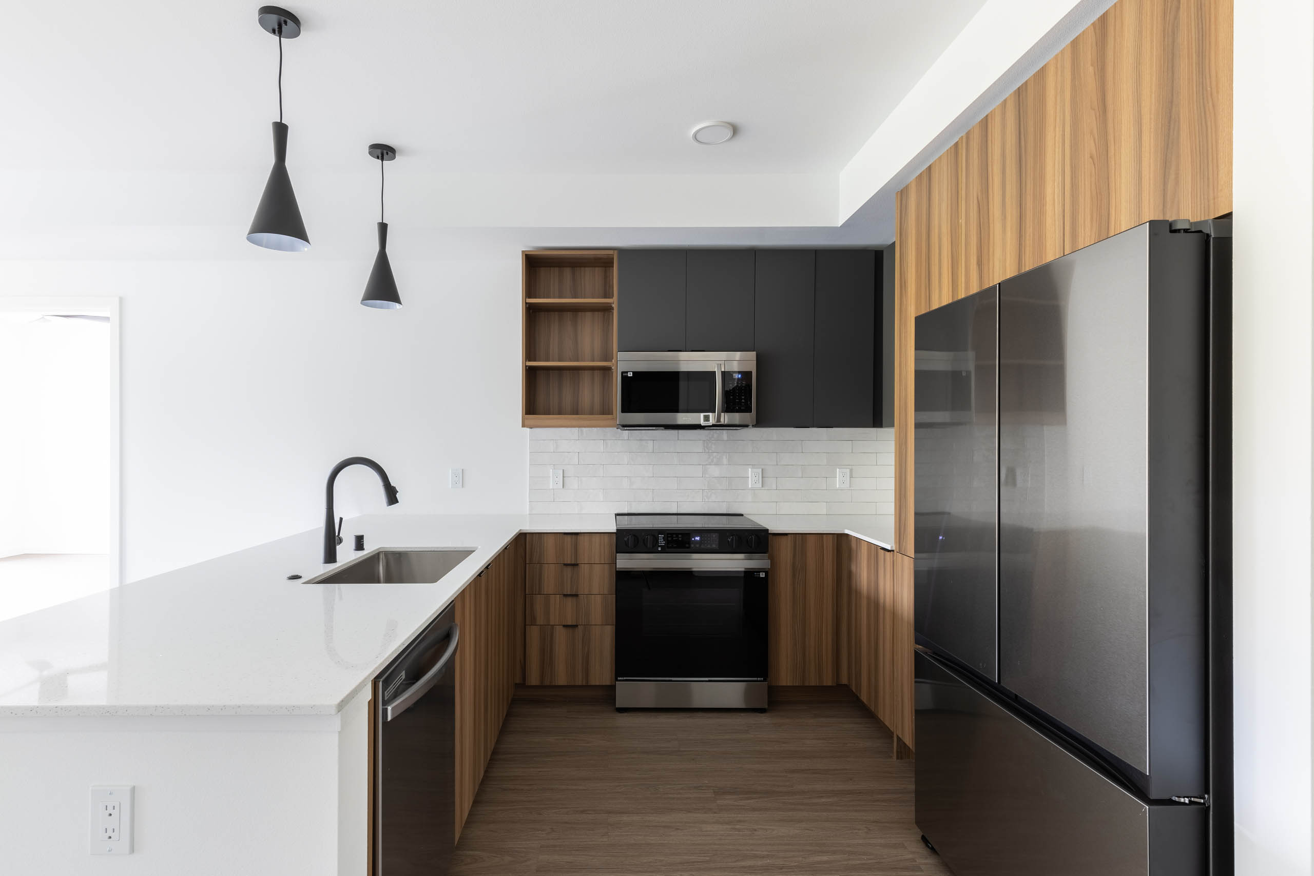Interior view of AMLI Redmond Way apartment kitchen with quartz countertops, black fixtures, and stainless appliances.