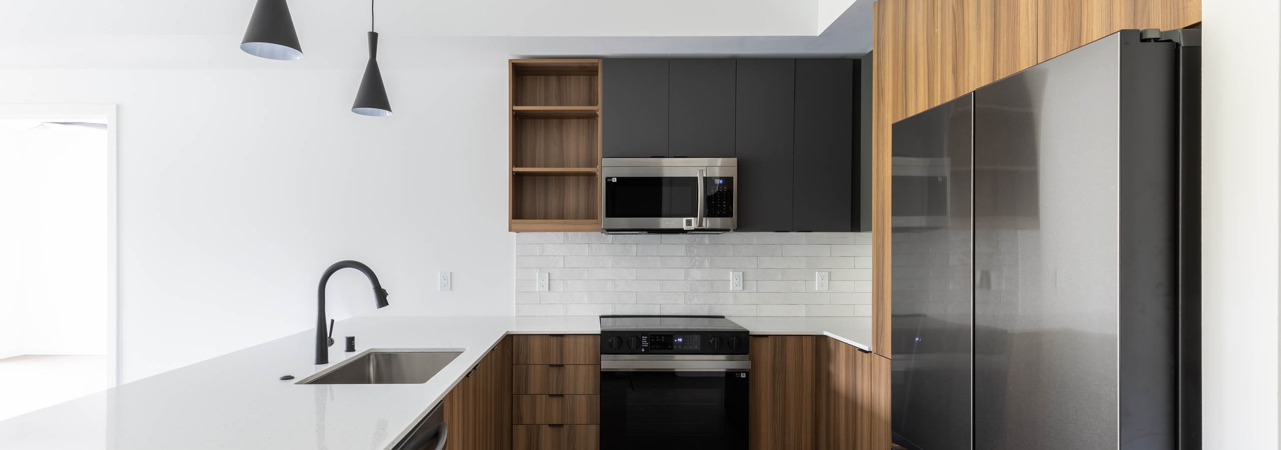 Interior view of AMLI Redmond Way apartment kitchen with quartz countertops, black fixtures, and stainless appliances.