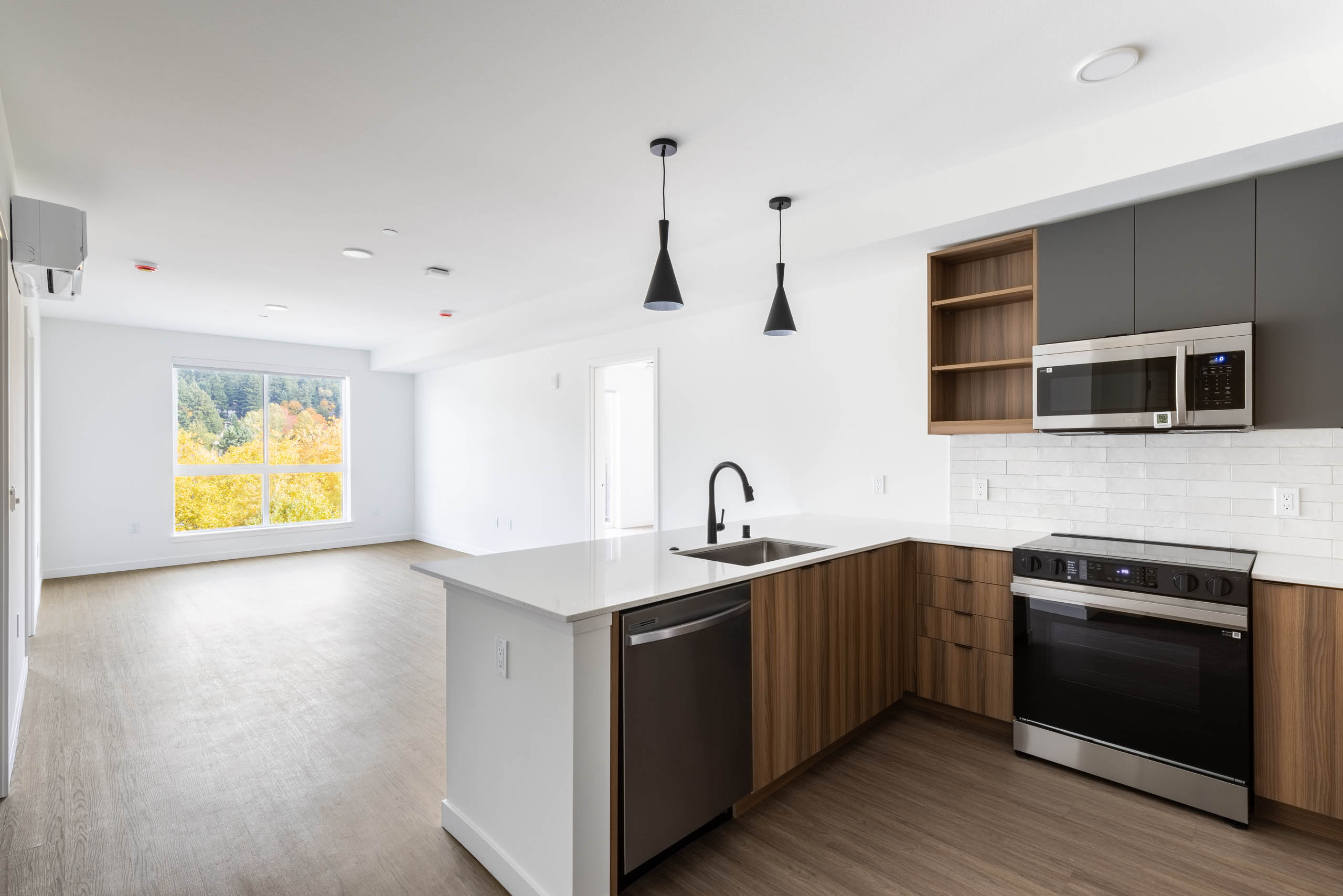 Wide view of AMLI Redmond Way apartment kitchen and living area with pendant lights, wood floors, and large window.
