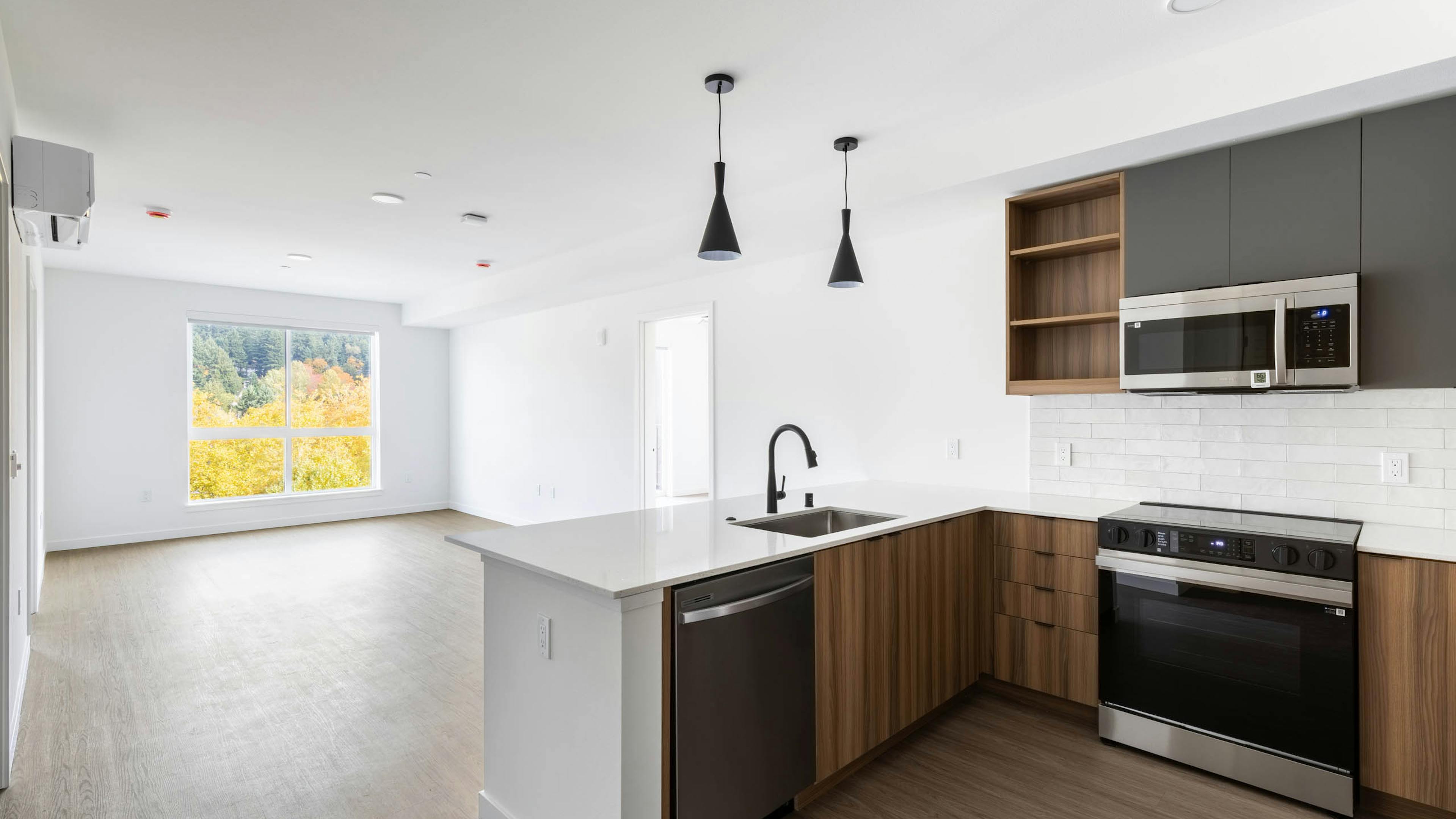Wide view of AMLI Redmond Way apartment kitchen and living area with pendant lights, wood floors, and large window.