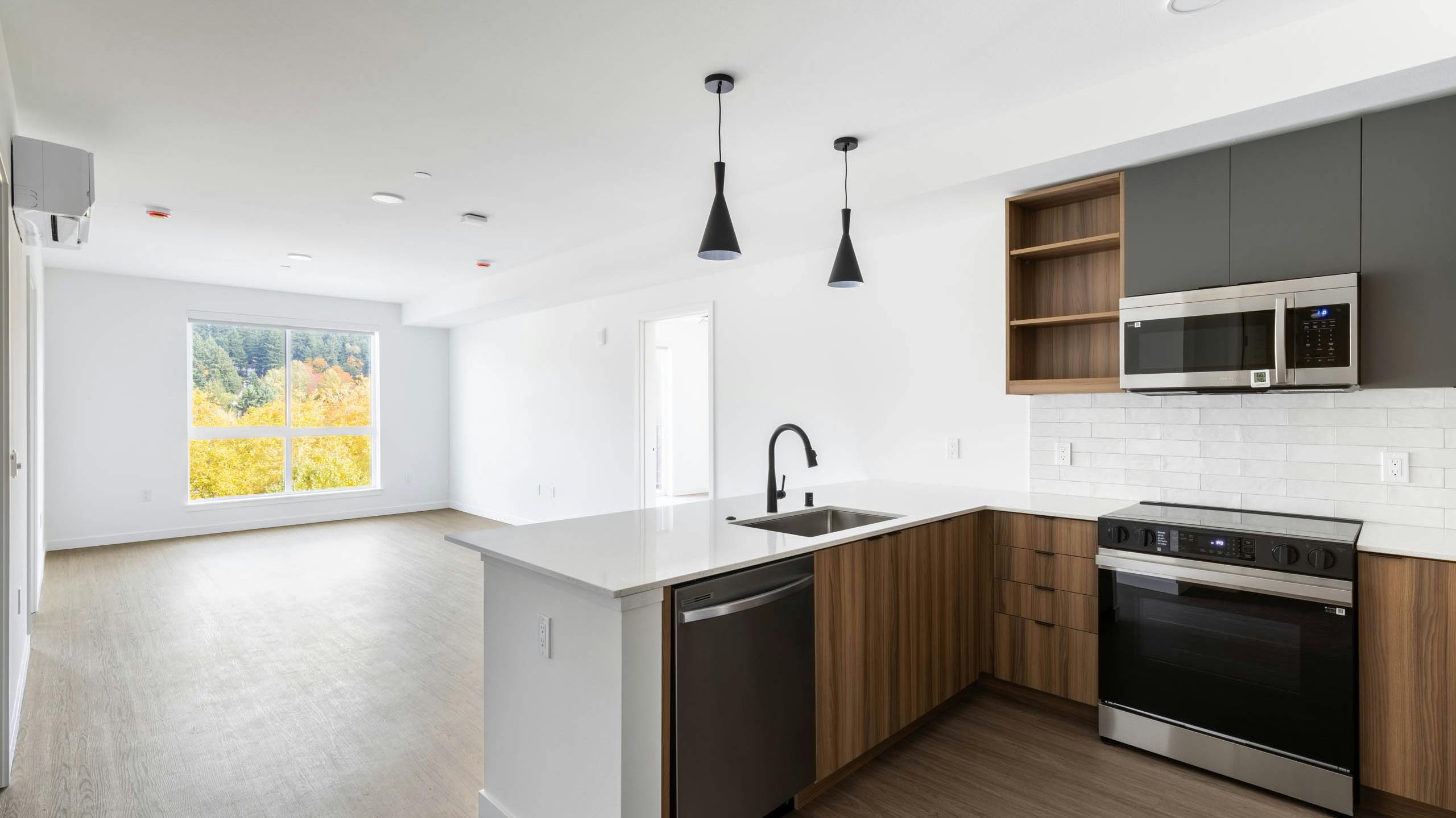 Wide view of AMLI Redmond Way apartment kitchen and living area with pendant lights, wood floors, and large window.