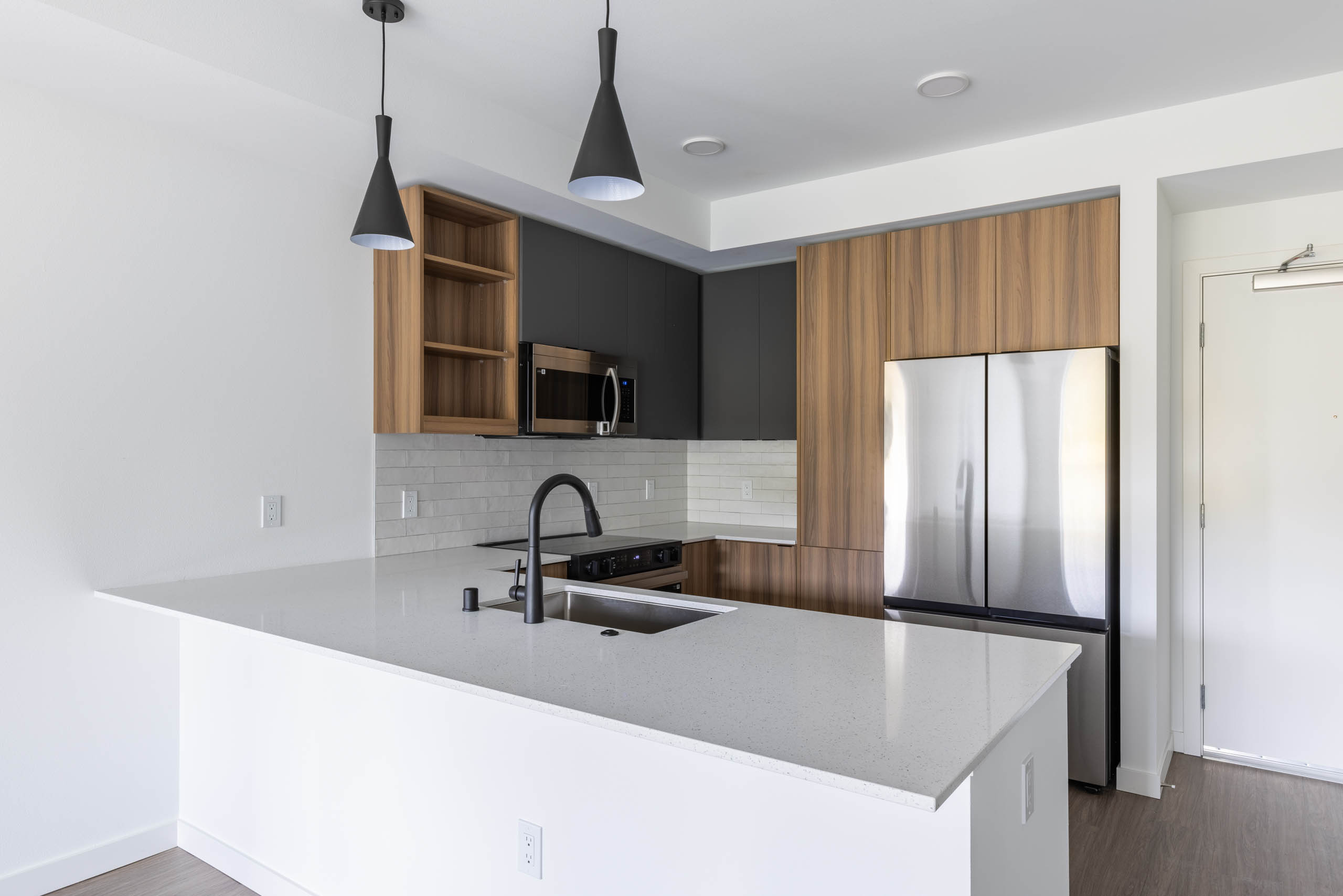 Angled view of apartment kitchen with black faucet, white quartz island, and modern wood cabinetry at AMLI Redmond Way.