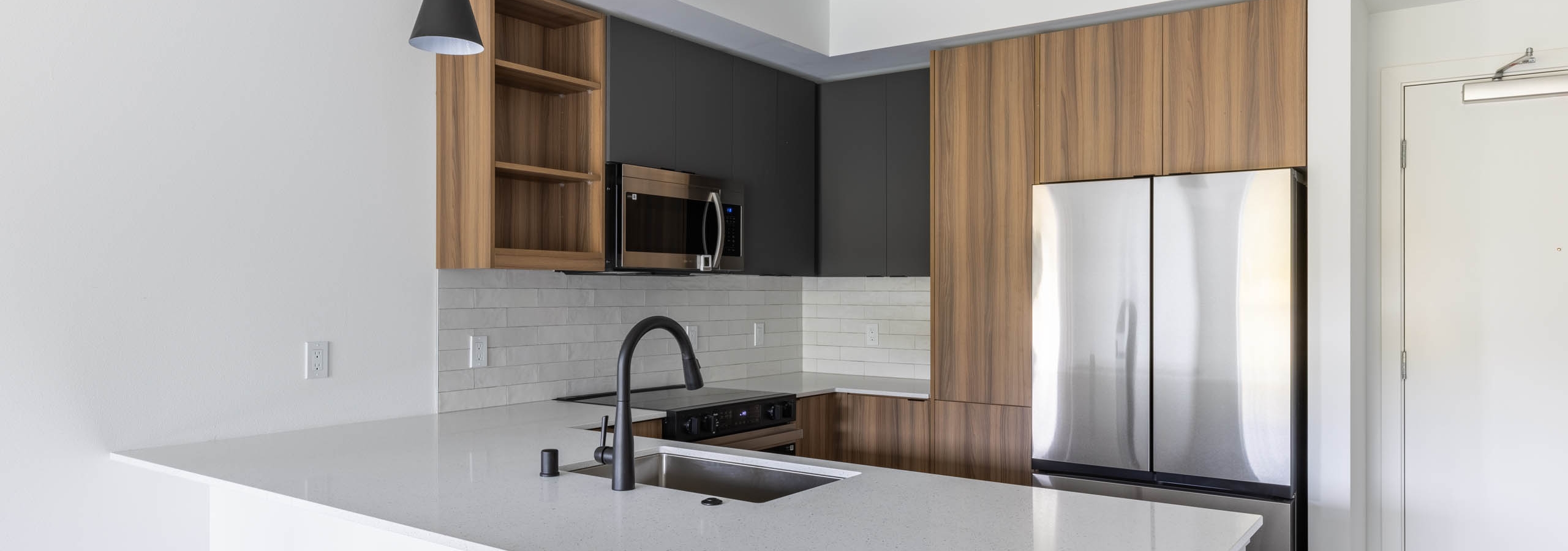 Angled view of apartment kitchen with black faucet, white quartz island, and modern wood cabinetry at AMLI Redmond Way.