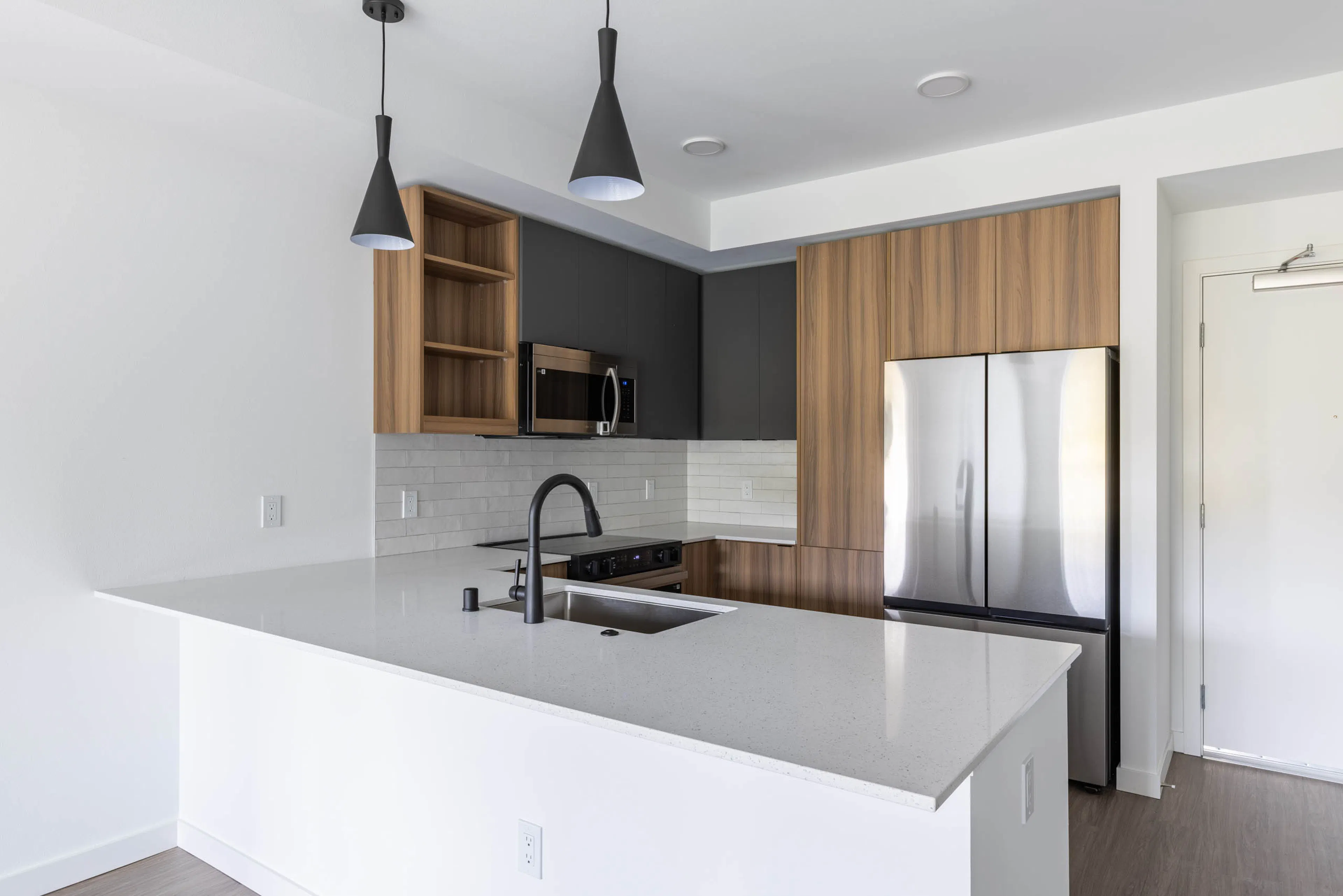 Angled view of apartment kitchen with black faucet, white quartz island, and modern wood cabinetry at AMLI Redmond Way.
