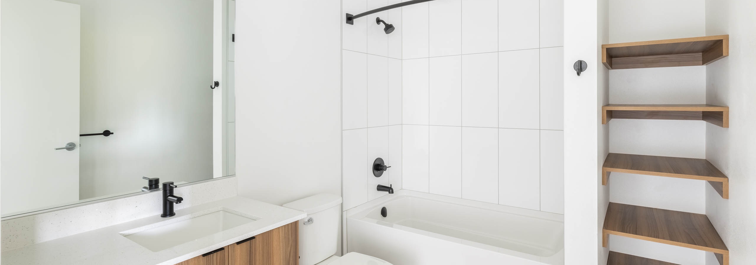 Interior view of AMLI Redmond Way apartment bathroom with large mirror, open shelving, and tub with white tile walls.