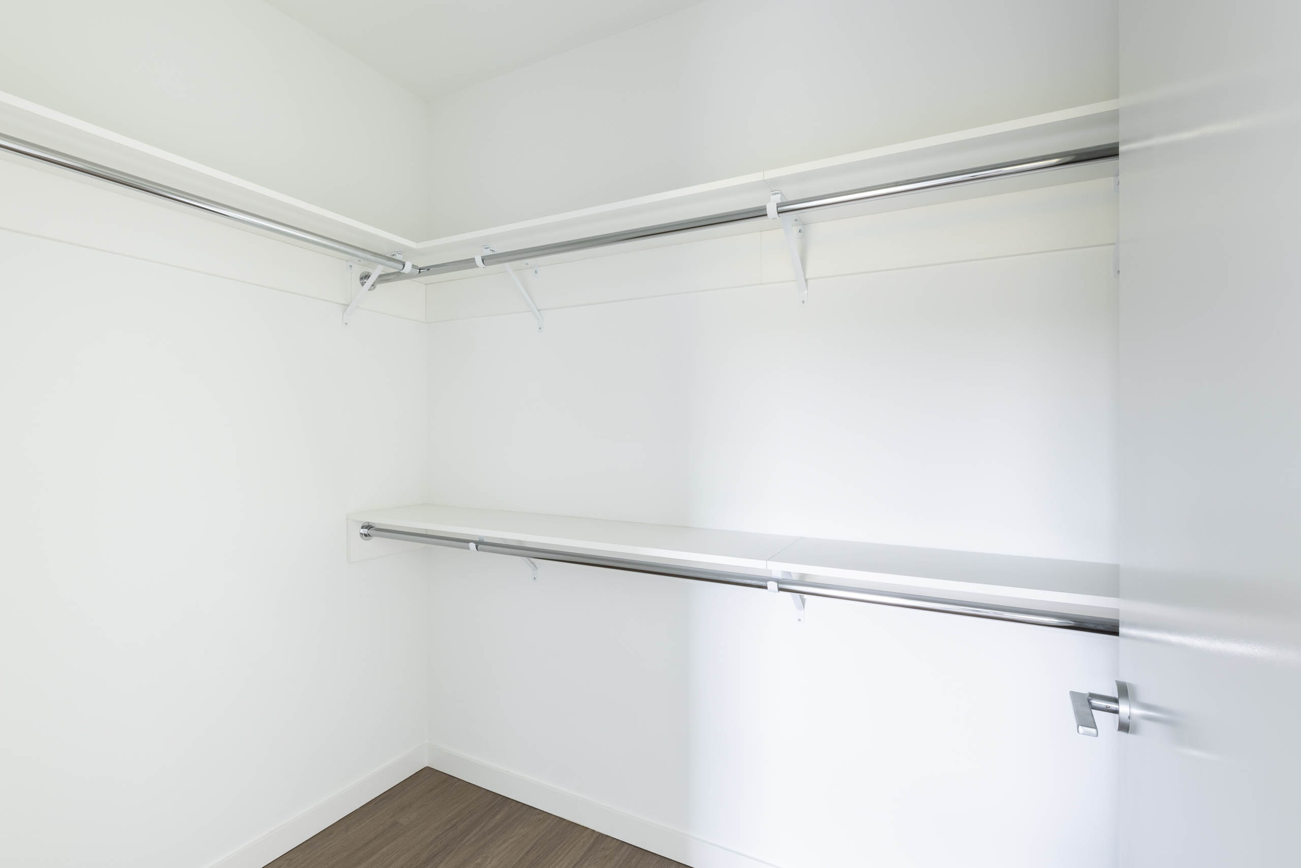 Interior view of AMLI Redmond Way apartment walk-in closet with dual hanging rods and white walls with wood flooring.