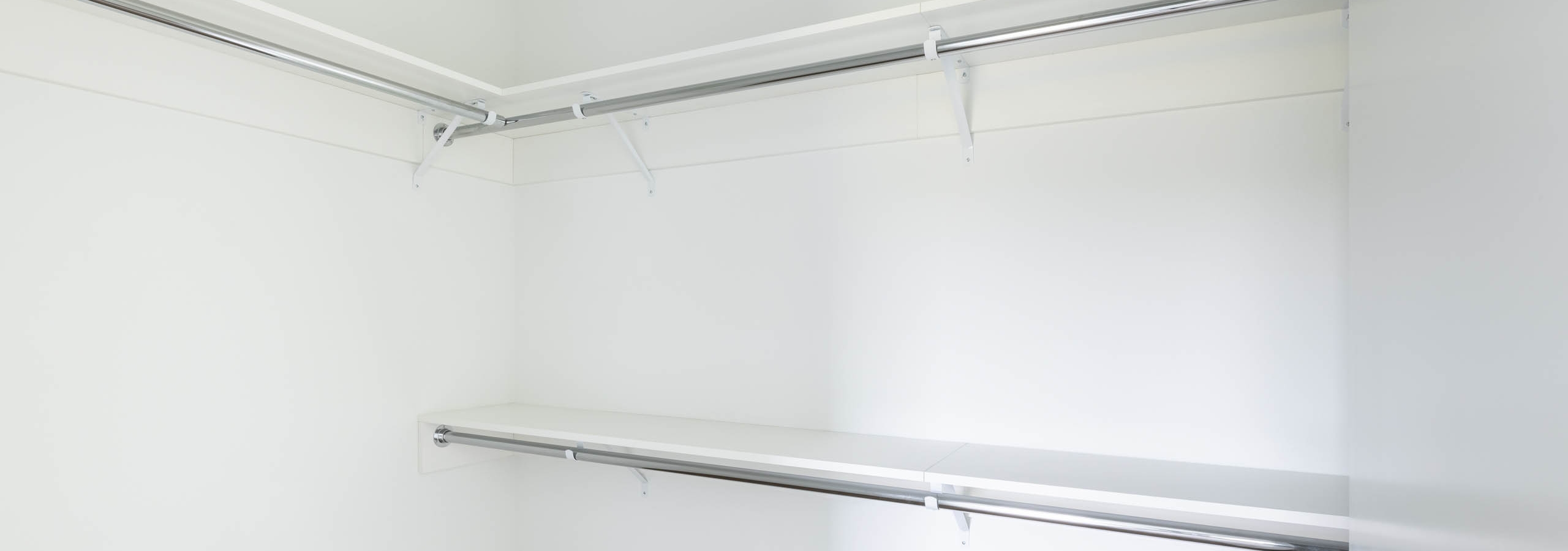 Interior view of AMLI Redmond Way apartment walk-in closet with dual hanging rods and white walls with wood flooring.
