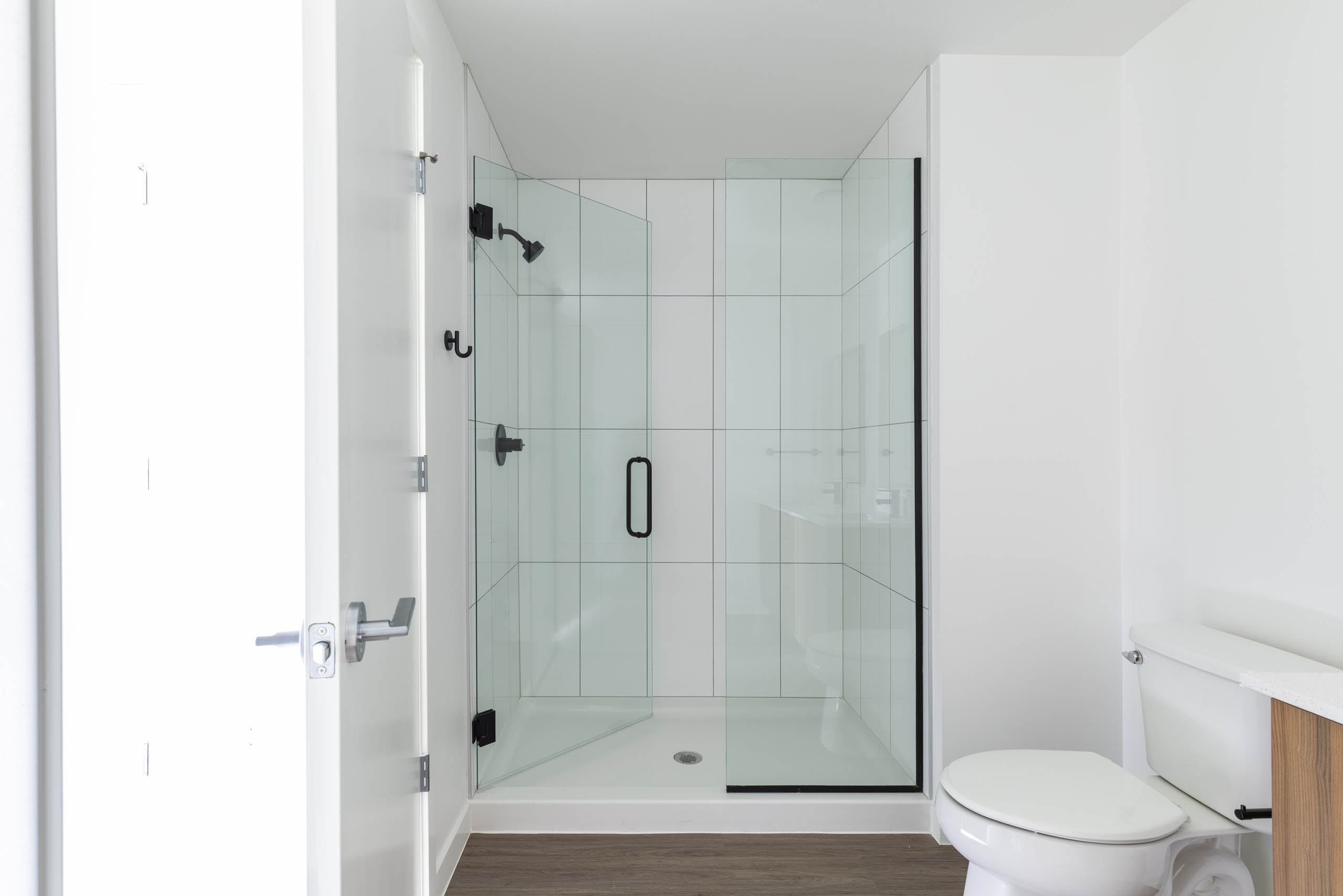 Interior view of AMLI Redmond Way apartment bathroom with glass walk-in shower with white tile walls and black fixtures.