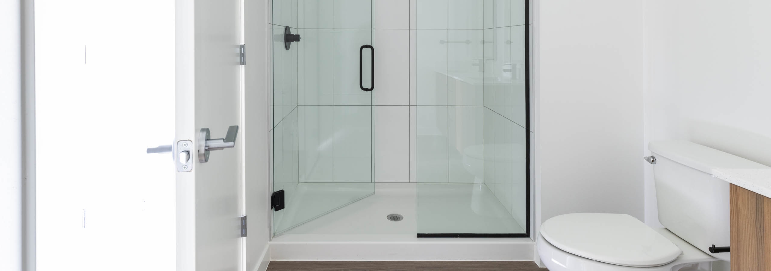 Interior view of AMLI Redmond Way apartment bathroom with glass walk-in shower with white tile walls and black fixtures.