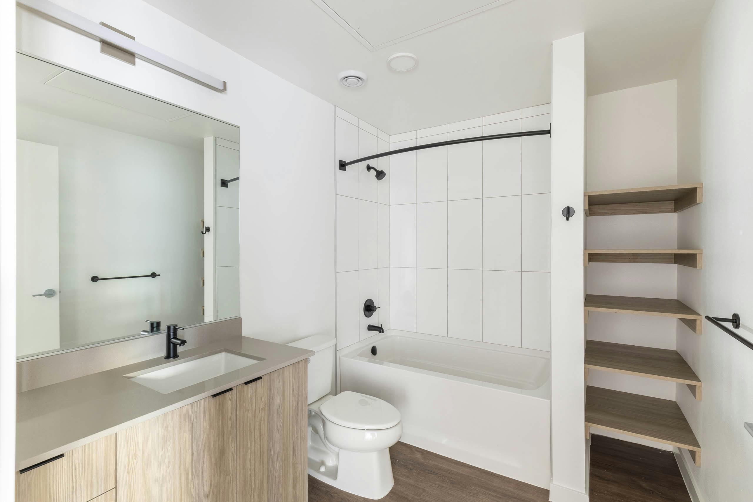 Interior view of AMLI Redmond Way apartment bathroom with soaking tub, open wood shelving, and large mirror with modern vanity.