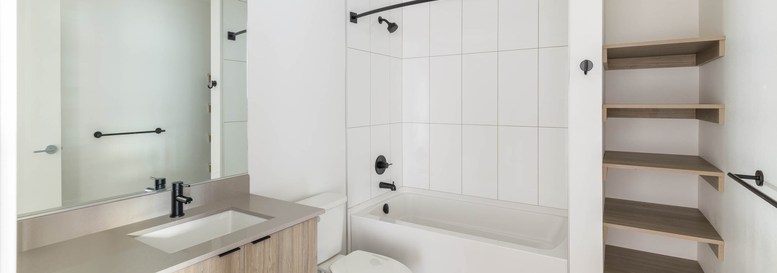 Interior view of AMLI Redmond Way apartment bathroom with soaking tub, open wood shelving, and large mirror with modern vanity.