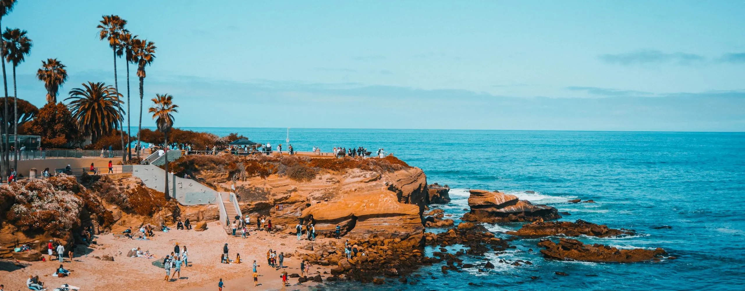 People walking and relaxing on a sunny La Jolla beach during the day.