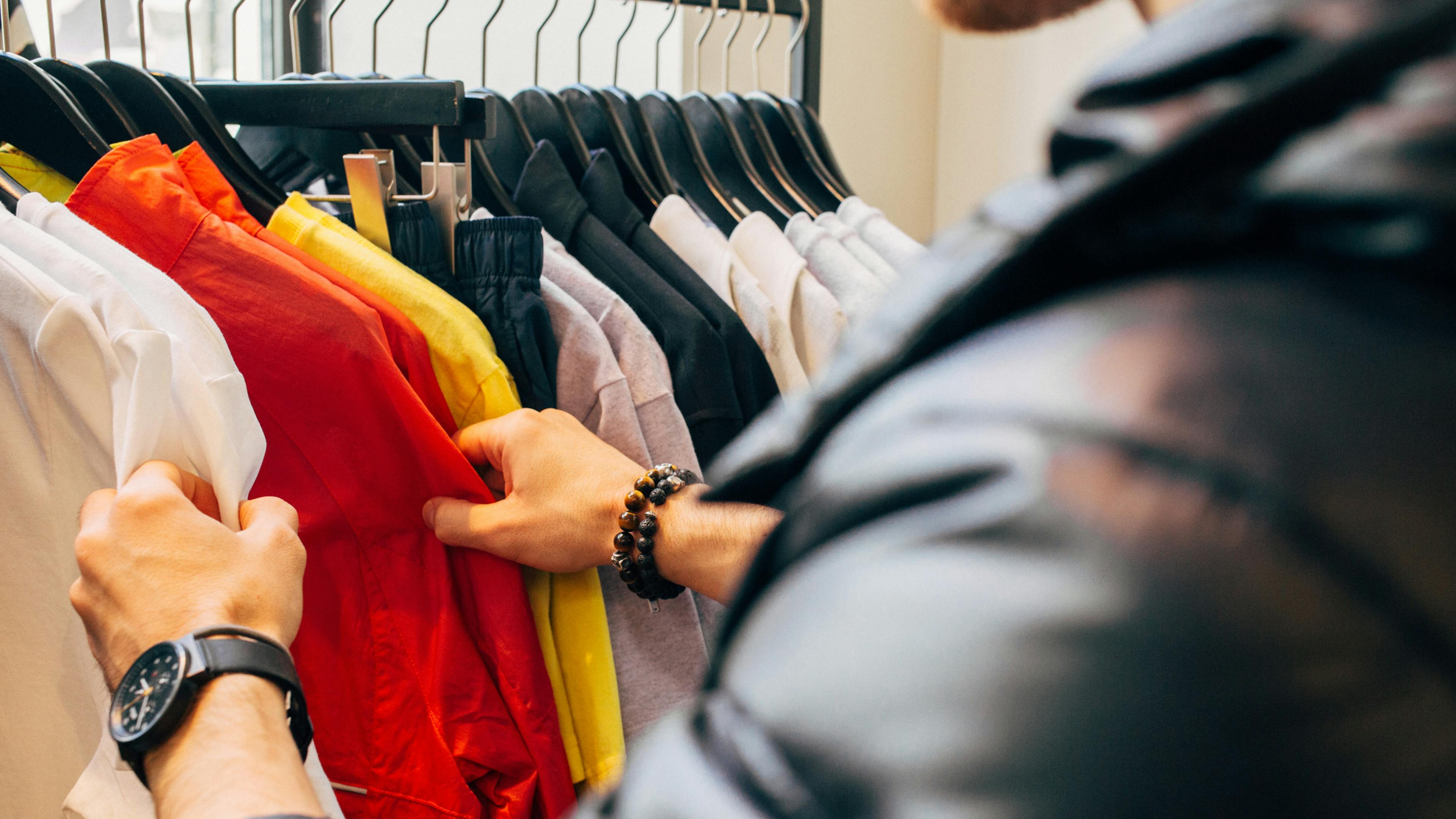 Rear view of person looking through a hanging rack of clothes in a store