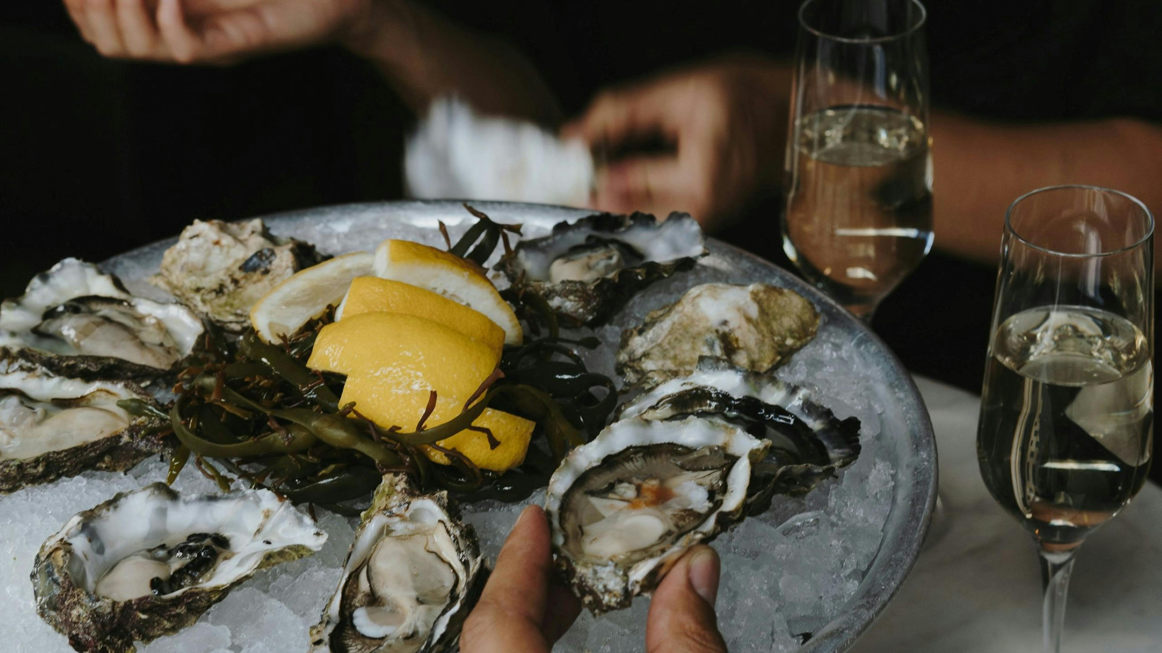 Person holding a plate of oysters with lemon wedges and a glasses of champagne.