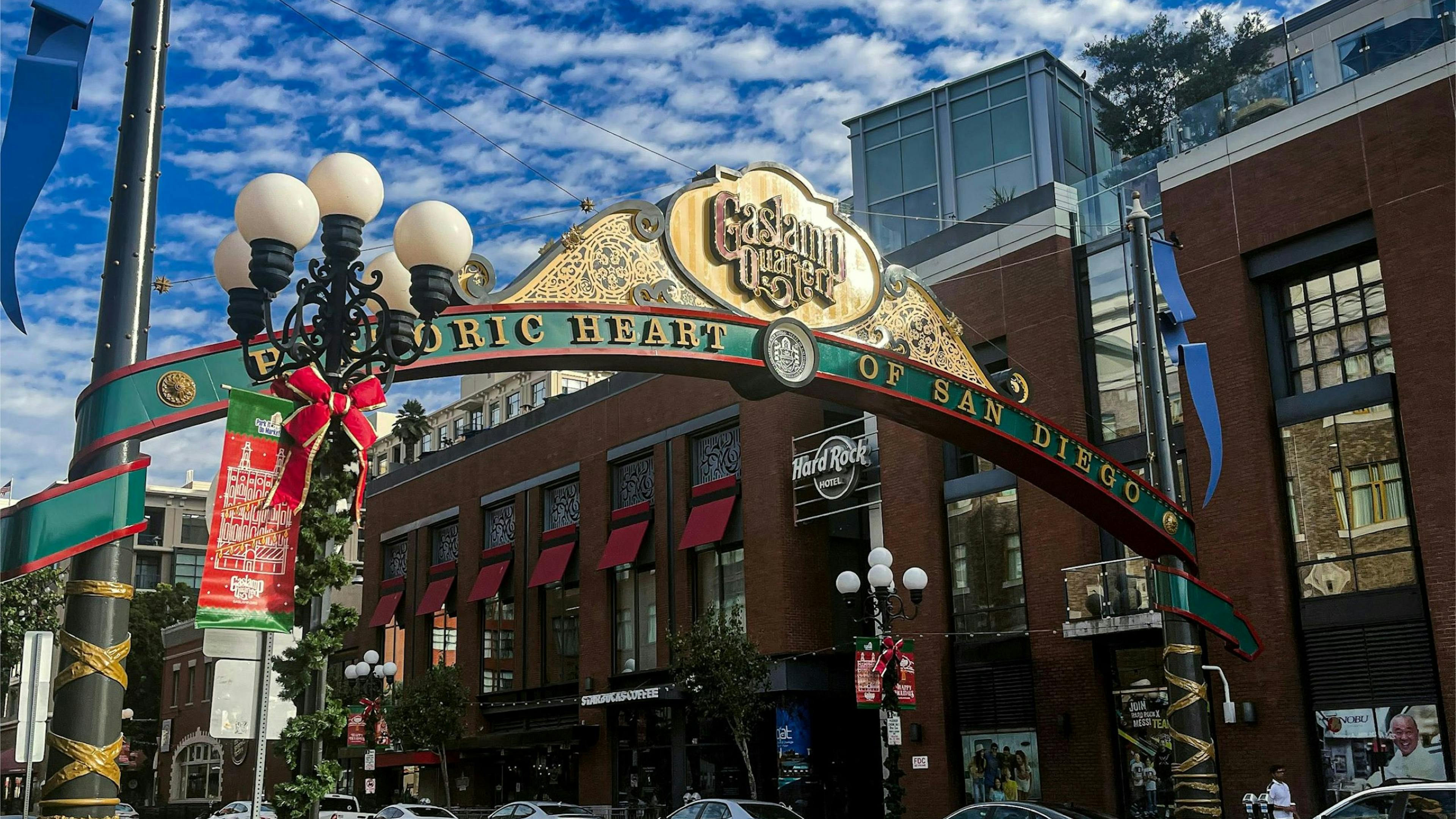 Gaslamp Quarter arch in downtown San Diego on a sunny day, with cars, shops, and holiday street decorations.