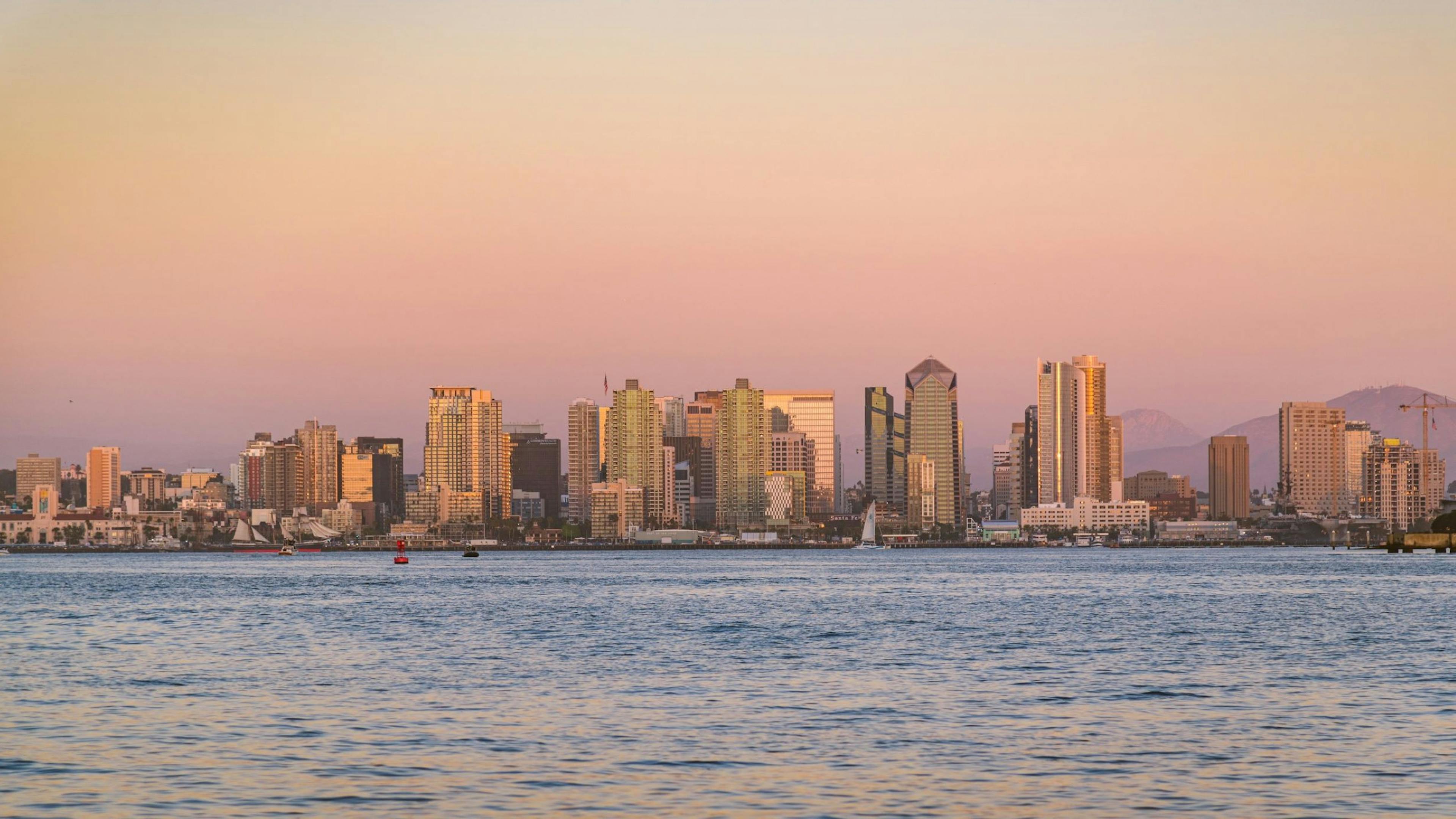 San Diego skyline at sunset seen from the water, with glowing high-rises and colorful sky.