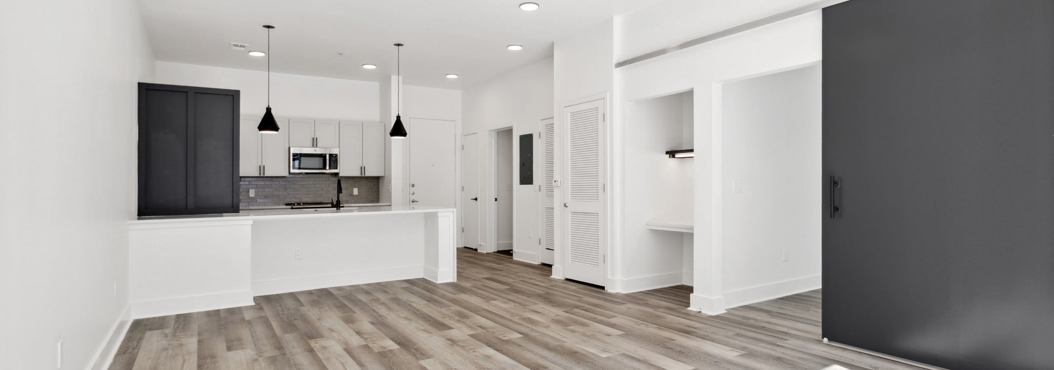 View of living room with gray floors and a black barn bedroom door and kitchen with two toned cabinets and peninsula at AMLI Old 4th Ward