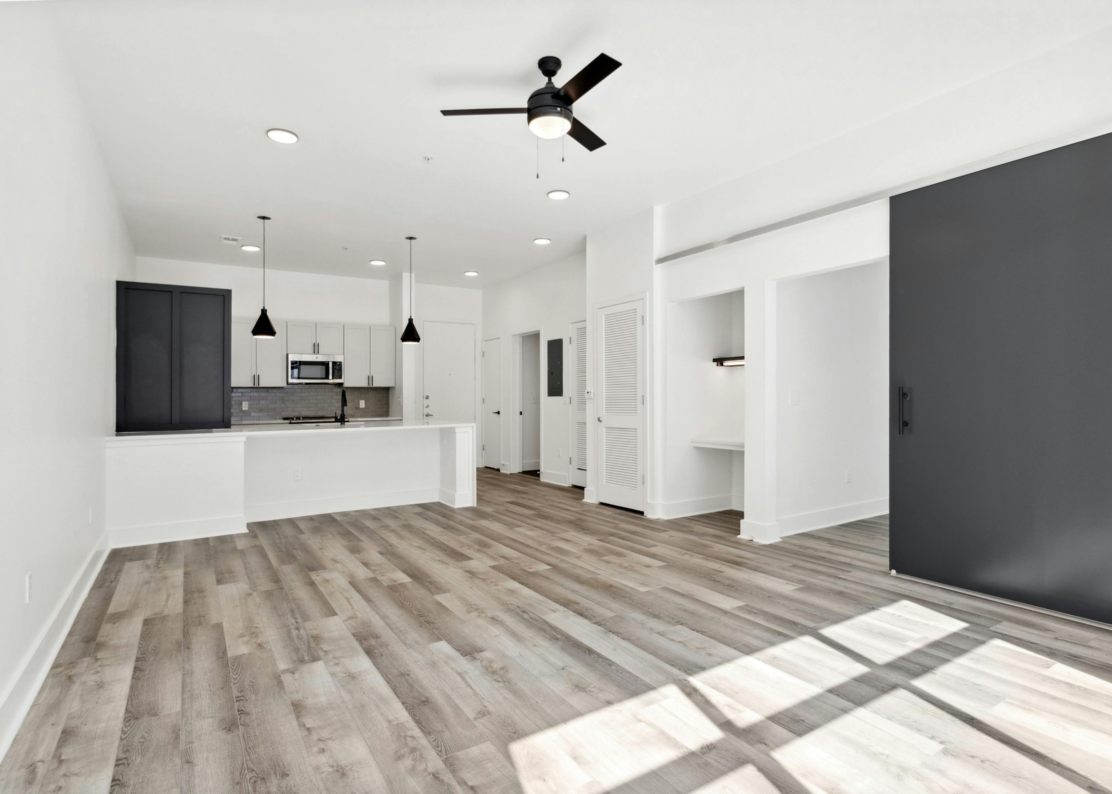 View of living room with gray floors and a black barn bedroom door and kitchen with two toned cabinets and peninsula at AMLI Old 4th Ward