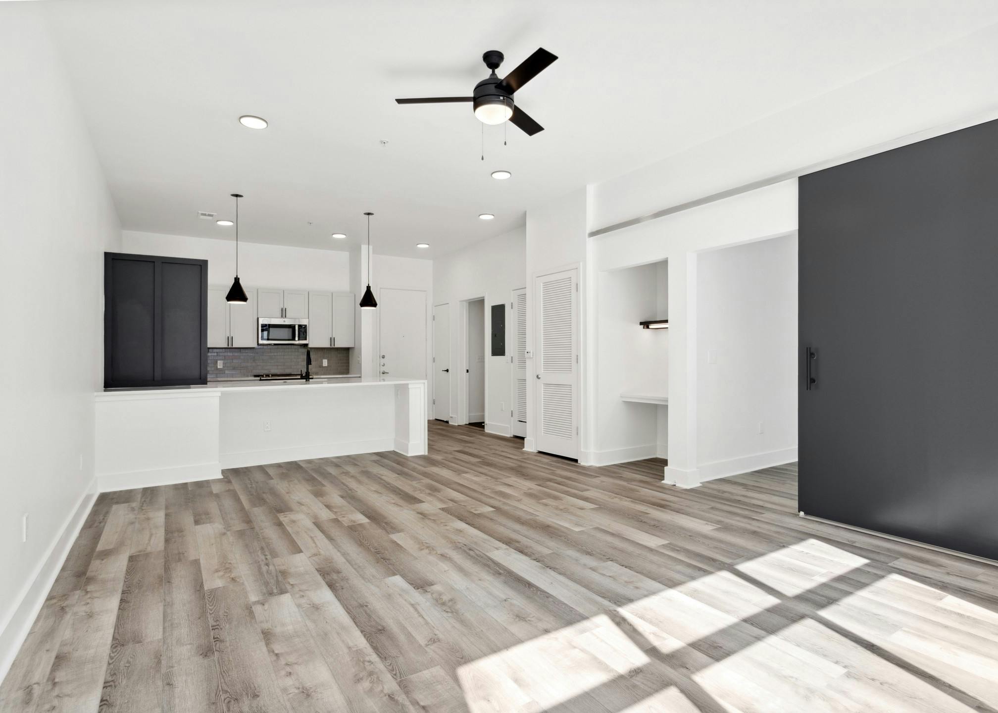 View of living room with gray floors and a black barn bedroom door and kitchen with two toned cabinets and peninsula at AMLI Old 4th Ward