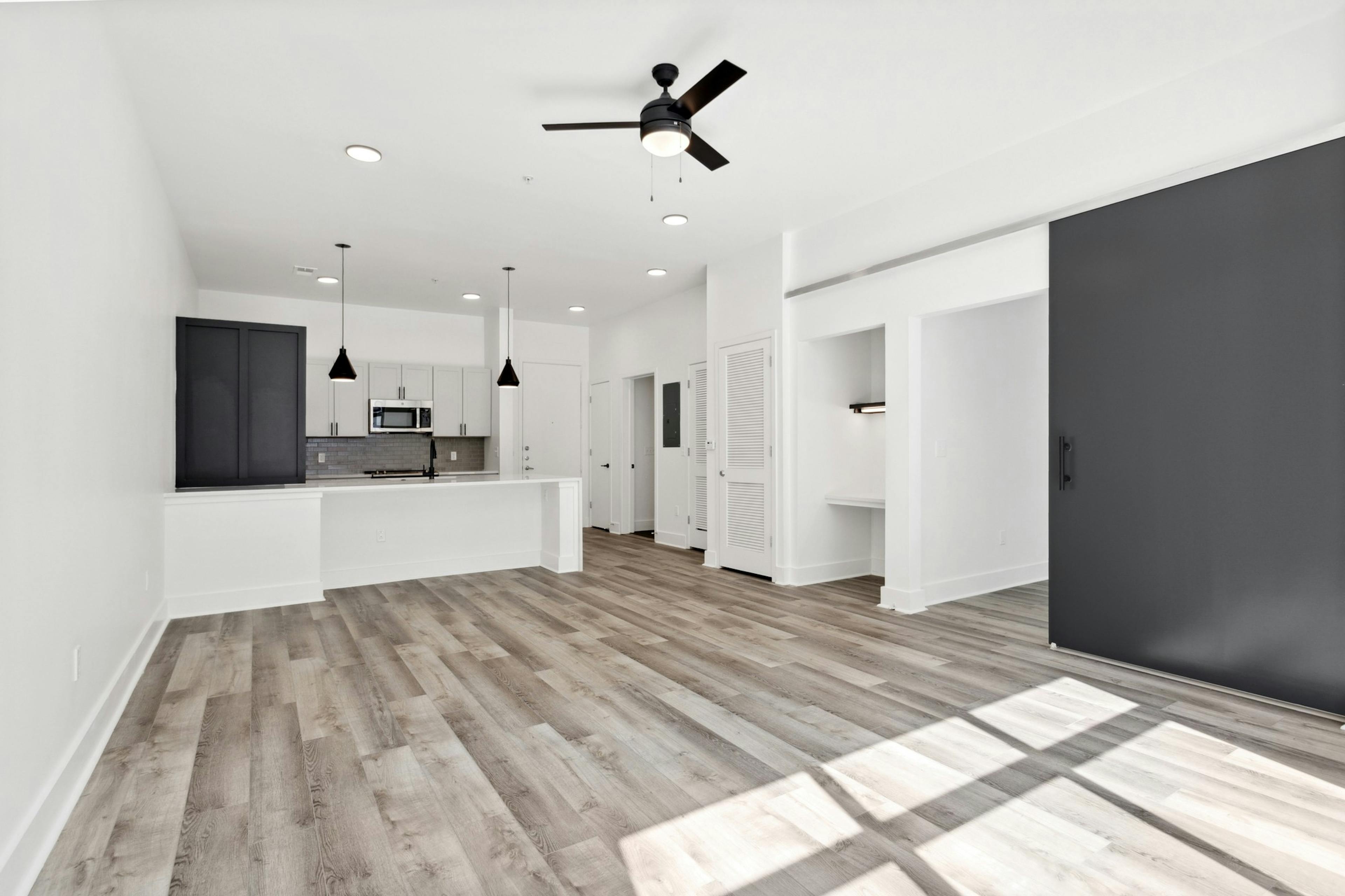 View of living room with gray floors and a black barn bedroom door and kitchen with two toned cabinets and peninsula at AMLI Old 4th Ward