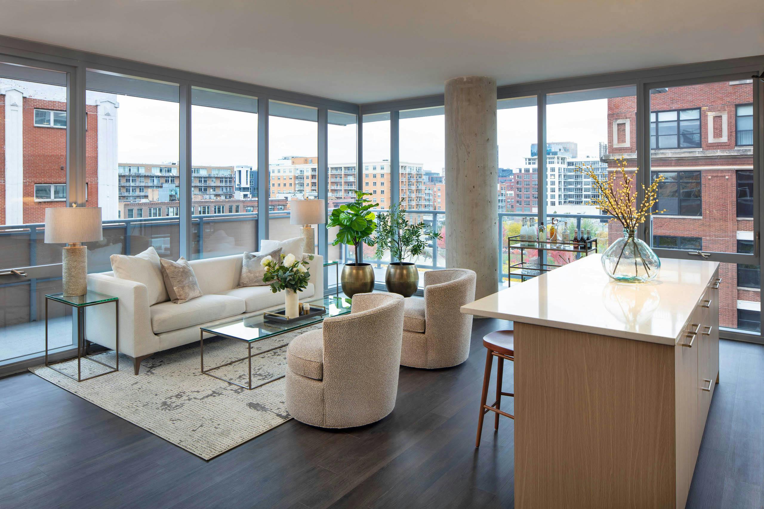 Living room with a white sofa, two textured chairs, a kitchen island, dark flooring, and floor-to-ceiling windows with a city view at AMLI West Loop