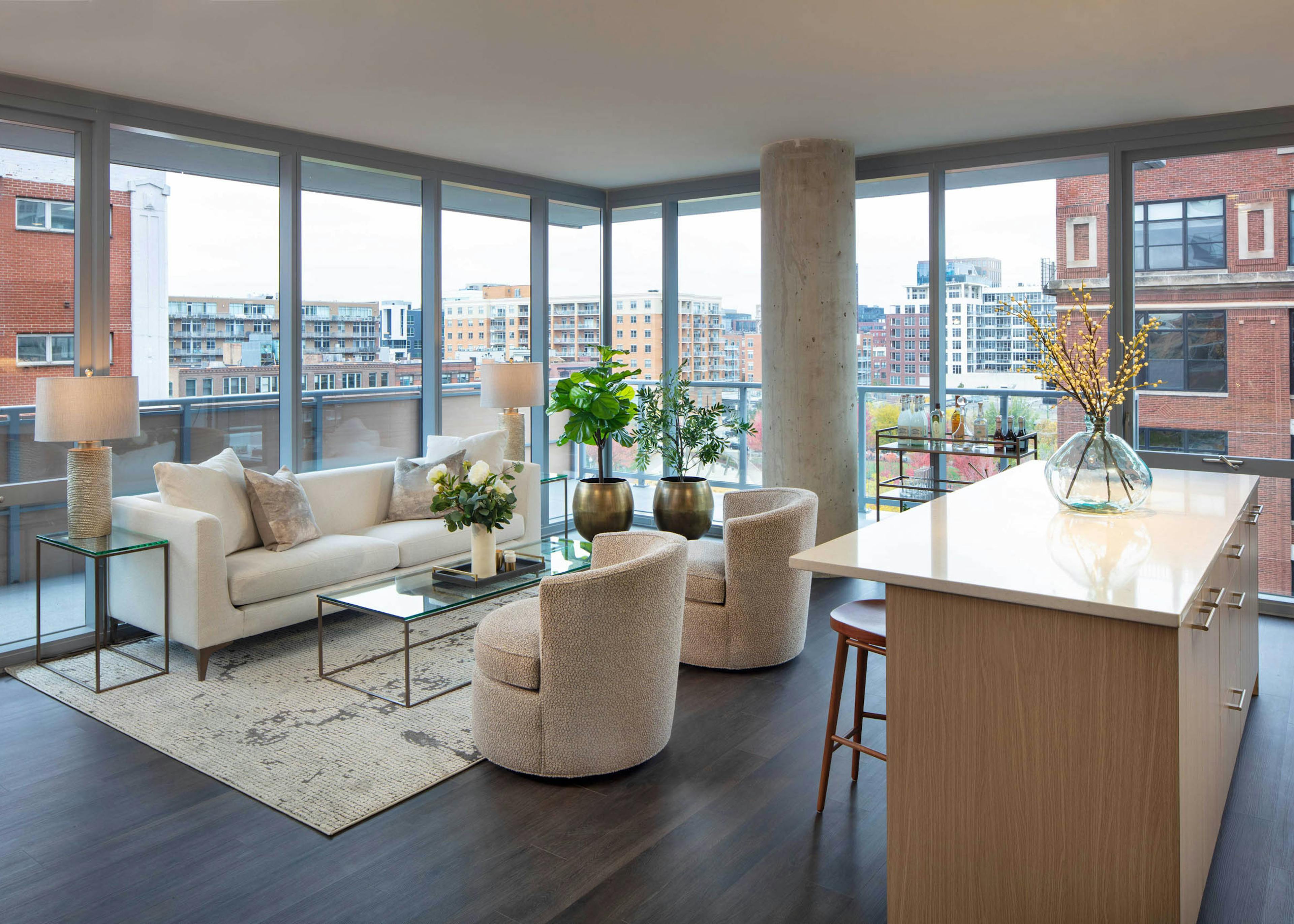 Living room with a white sofa, two textured chairs, a kitchen island, dark flooring, and floor-to-ceiling windows with a city view at AMLI West Loop