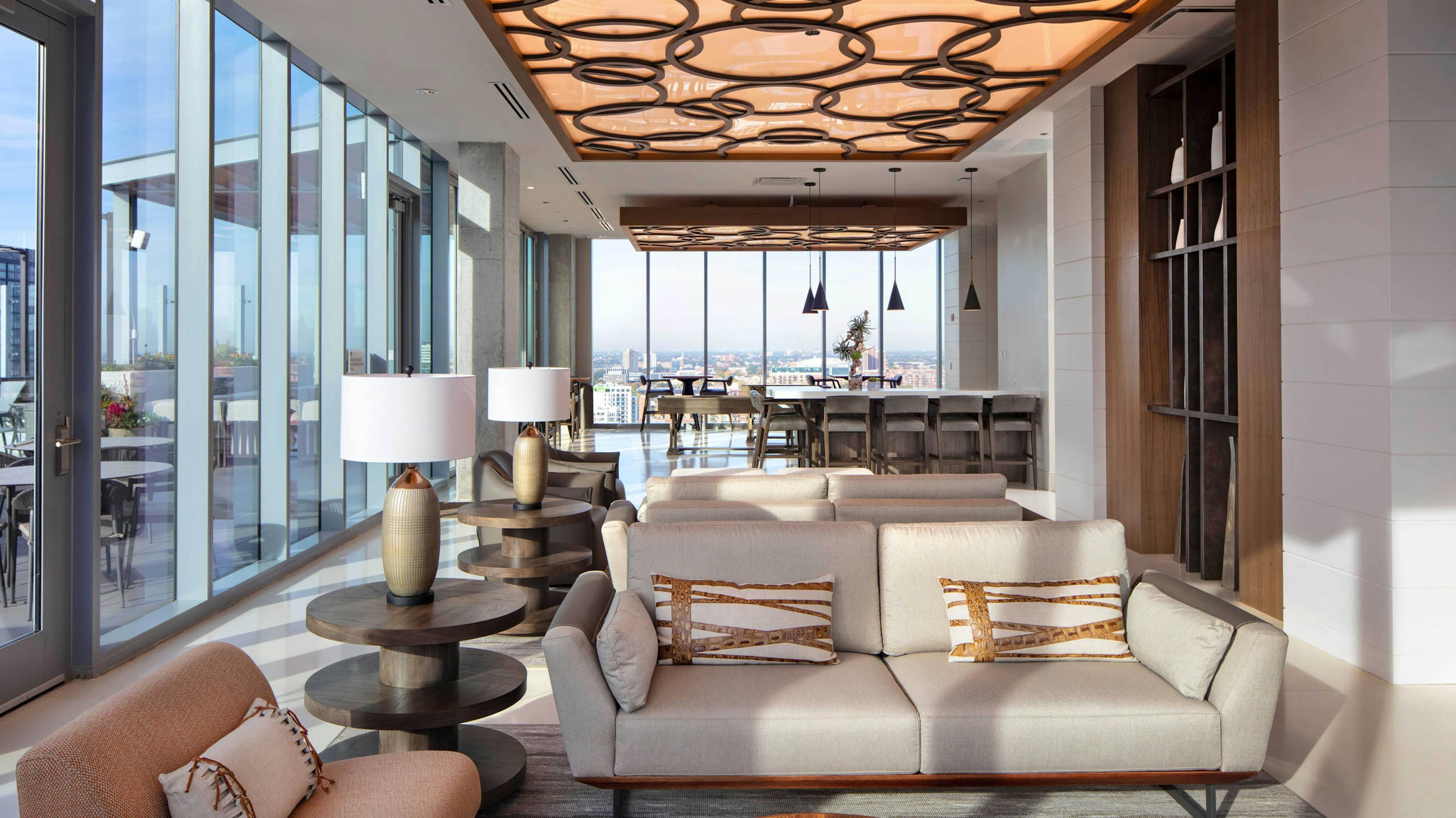 AMLI West Loop Resident Lounge featuring a sofa, armchairs, bar seating, and floor-to-ceiling windows with a city view.