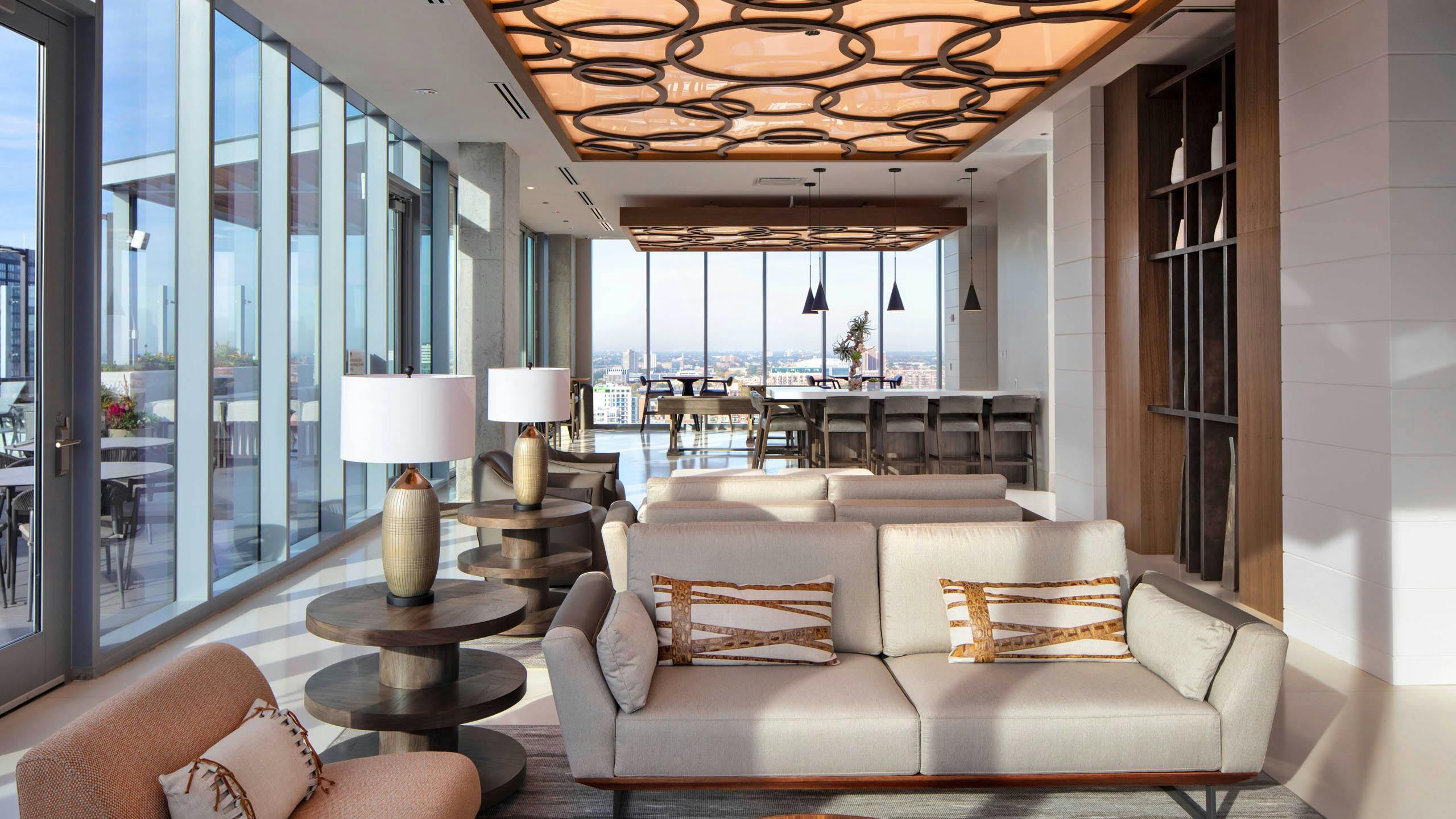 AMLI West Loop Resident Lounge featuring a sofa, armchairs, bar seating, and floor-to-ceiling windows with a city view.