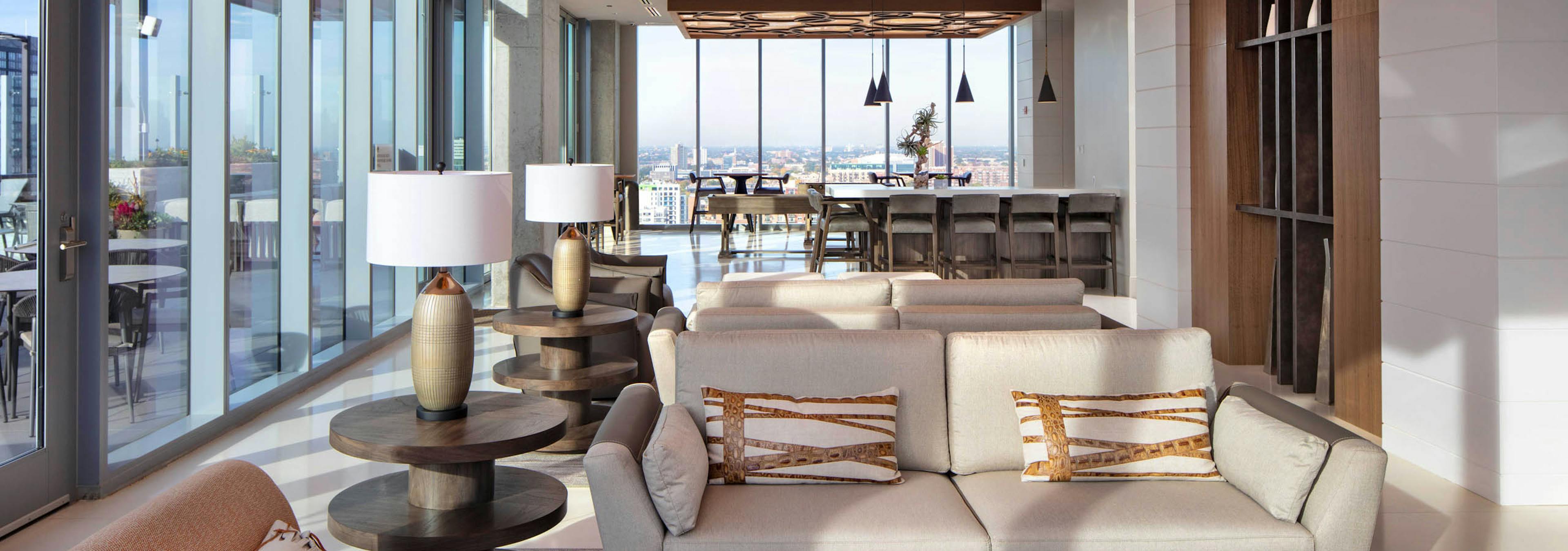 AMLI West Loop Resident Lounge featuring a sofa, armchairs, bar seating, and floor-to-ceiling windows with a city view.